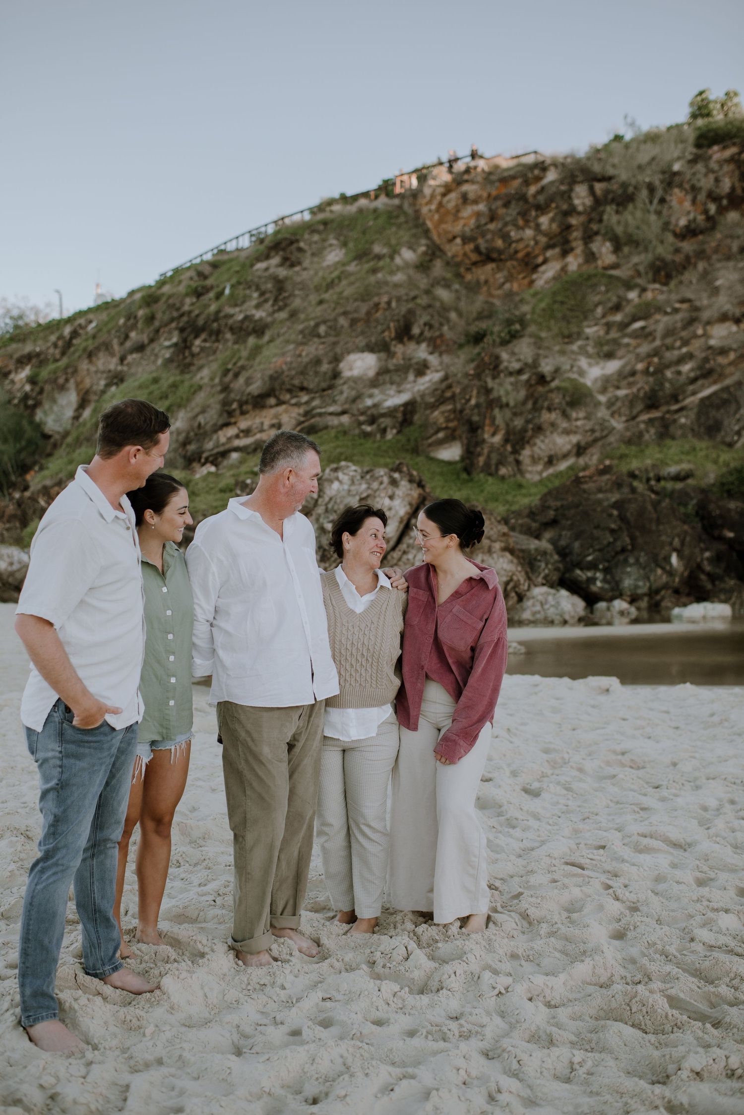 A small group stands together on a sandy beach with rocky cliffs in the background during golden hour.