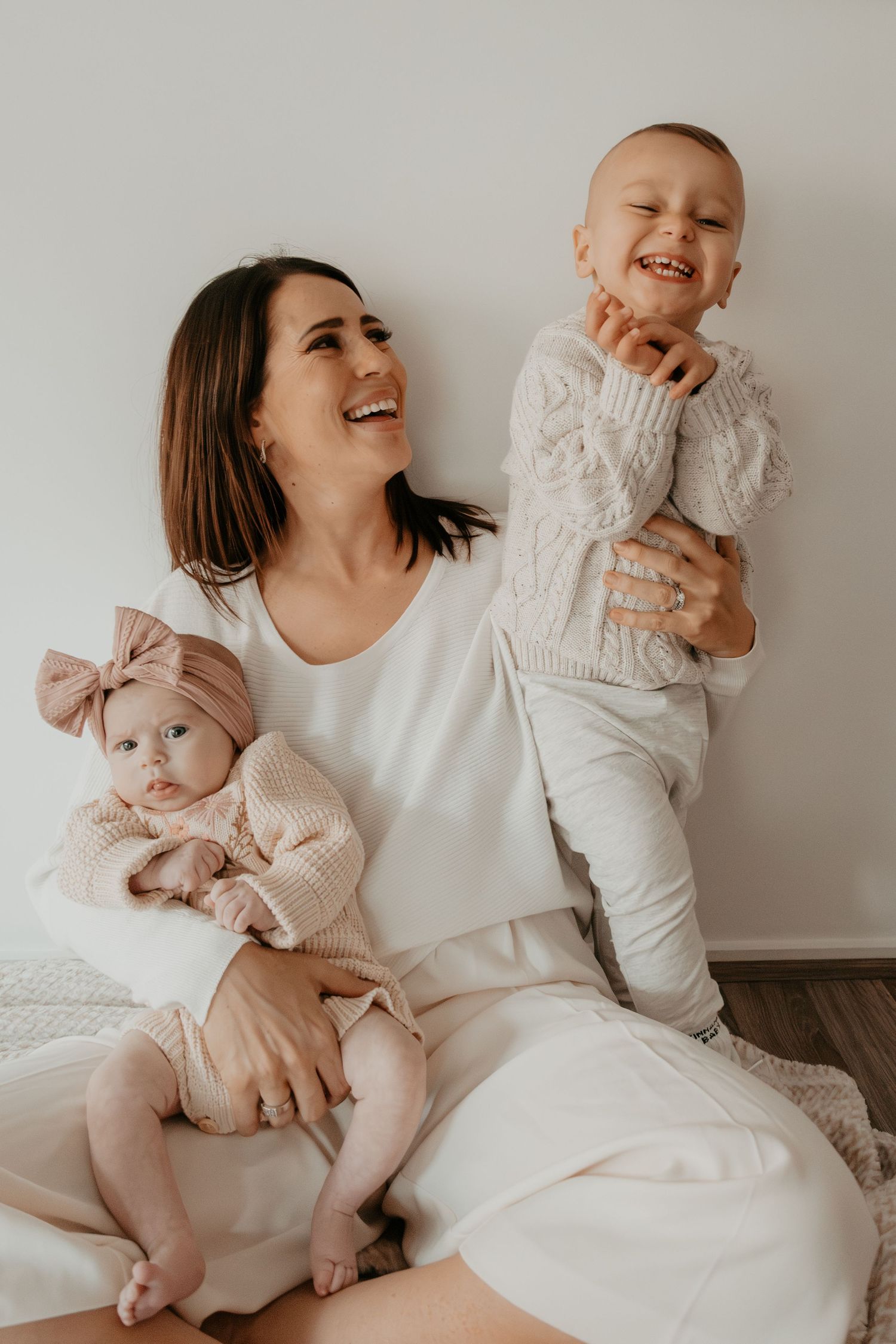 A joyful family moment features a parent and children in matching white outfits sitting together on a cozy floor.