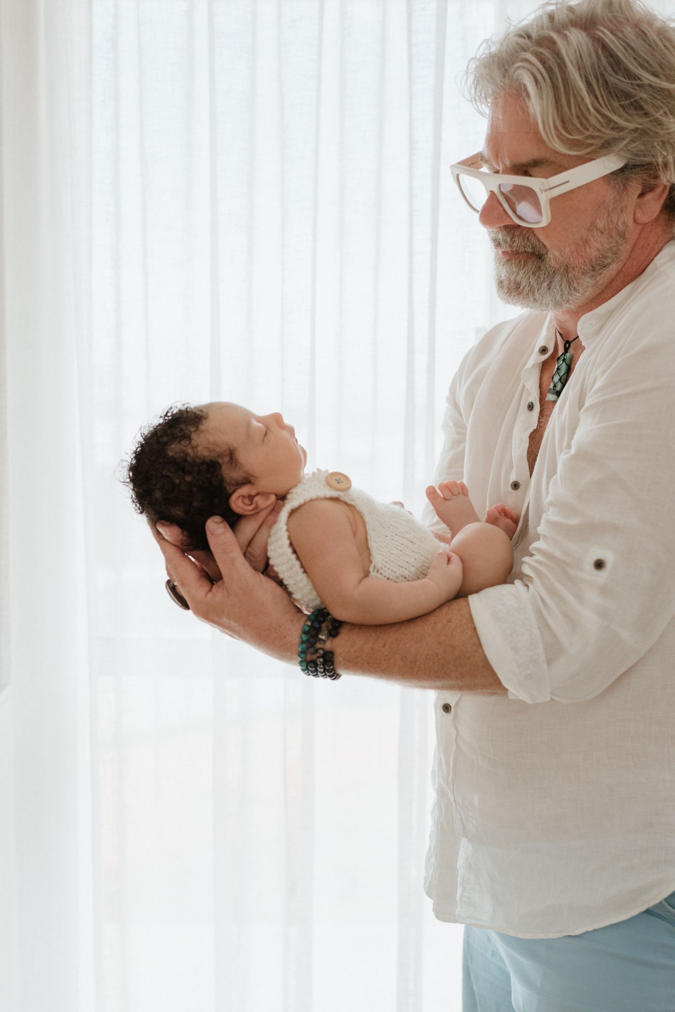 Person in white shirt tenderly holding small infant against bright window background.