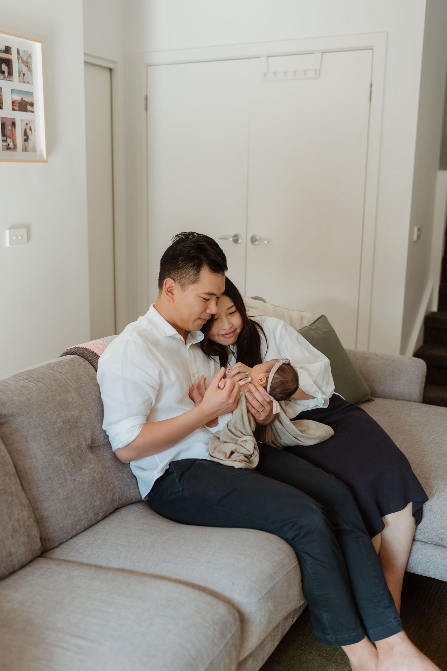 A couple shares intimate moments while sitting together on a gray couch in a minimalist white room.