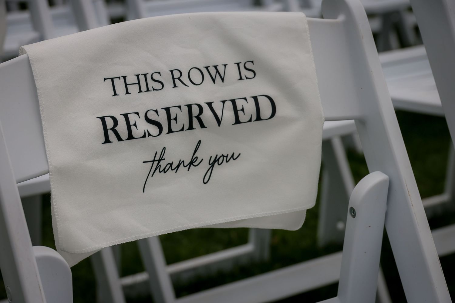White folding chair with a reserved row sign at a wedding ceremony outdoor seating arrangement.