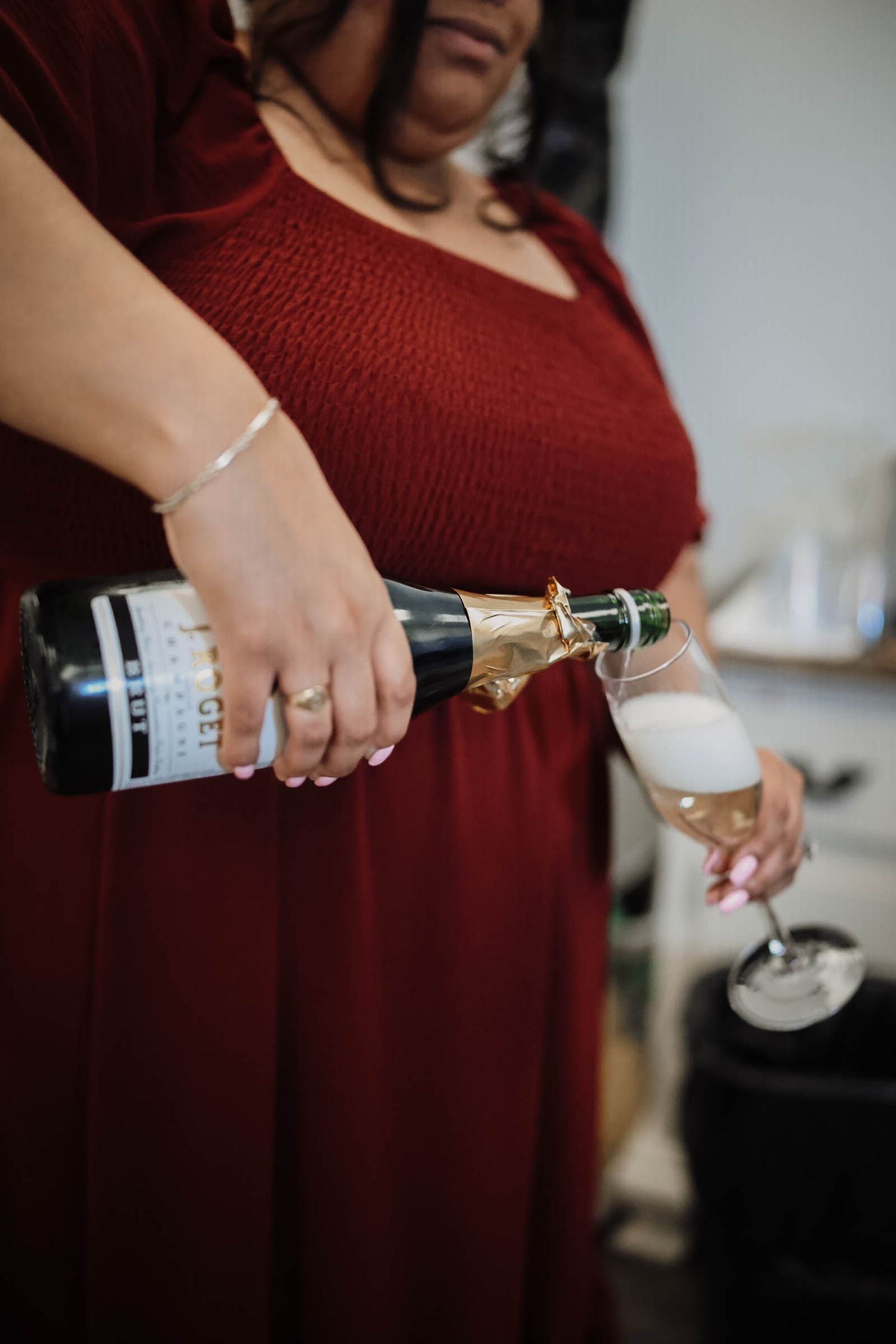 Woman in red dress pouring champagne into a flute glass, wearing silver bracelet and ring.