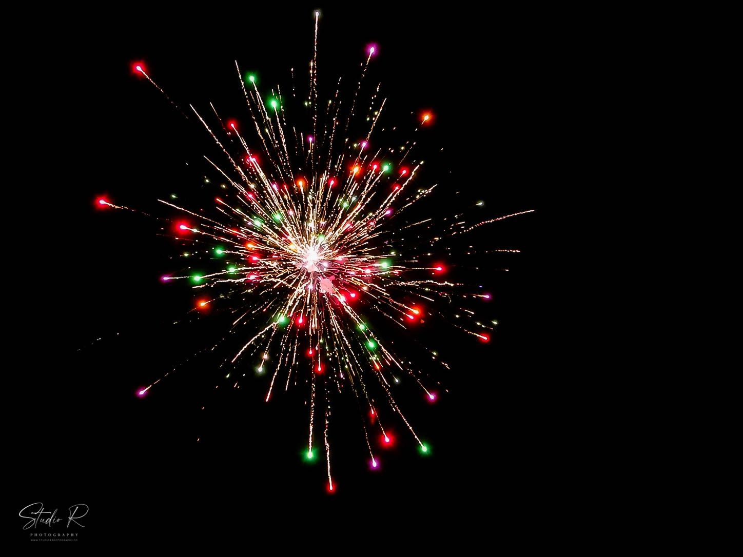 Vibrant red and green fireworks explode against a black night sky in a festive holiday display.