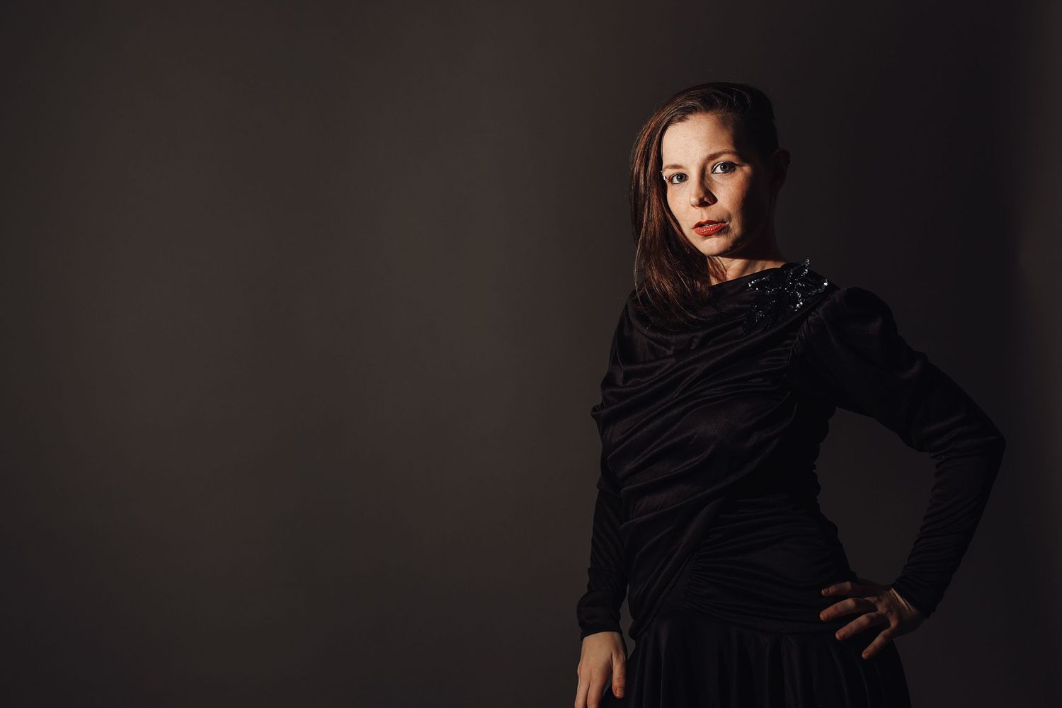Woman in black dress posing confidently against dark background in professional studio portrait photography.