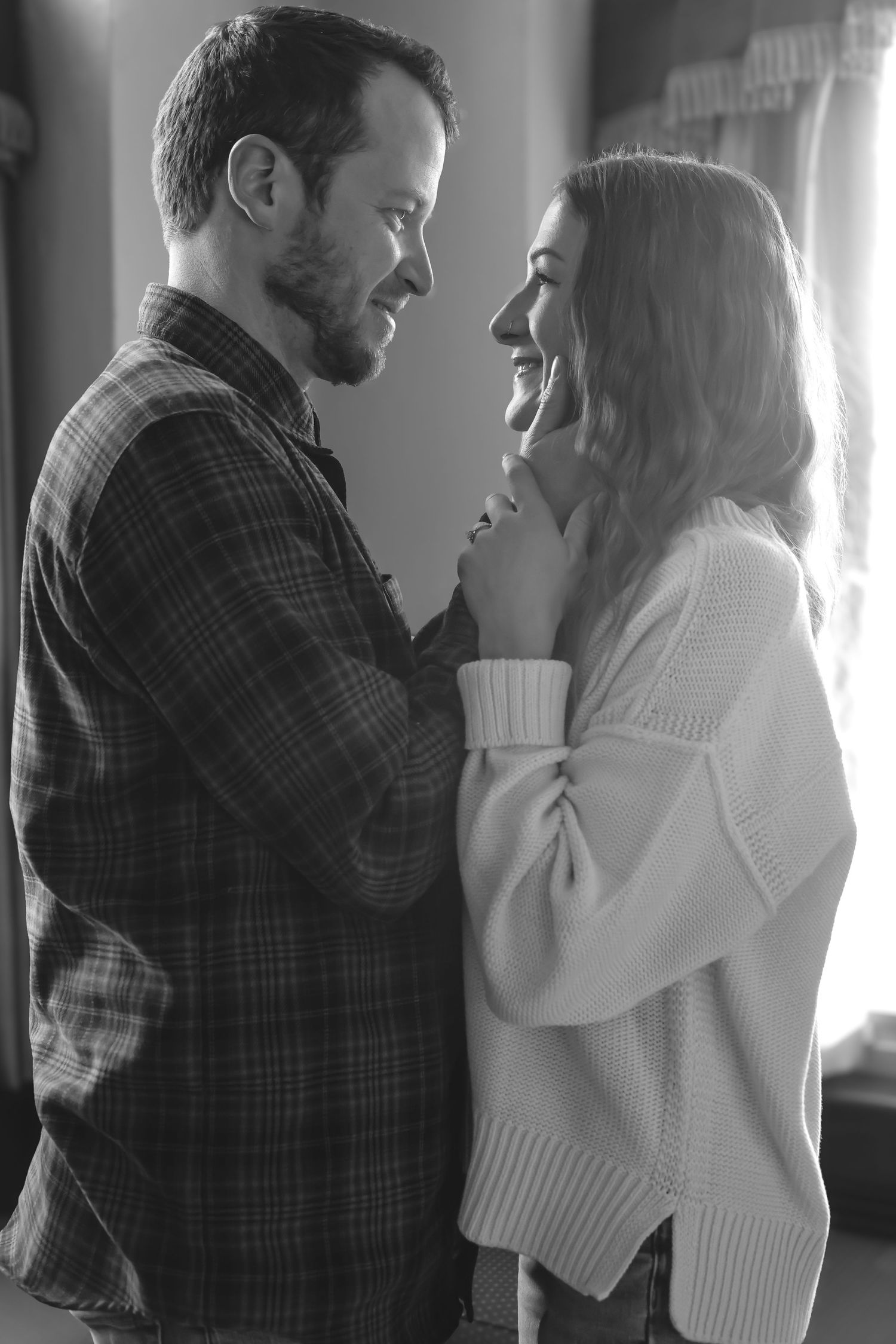 A romantic black and white portrait of a couple sharing an intimate moment in a cozy indoor setting.