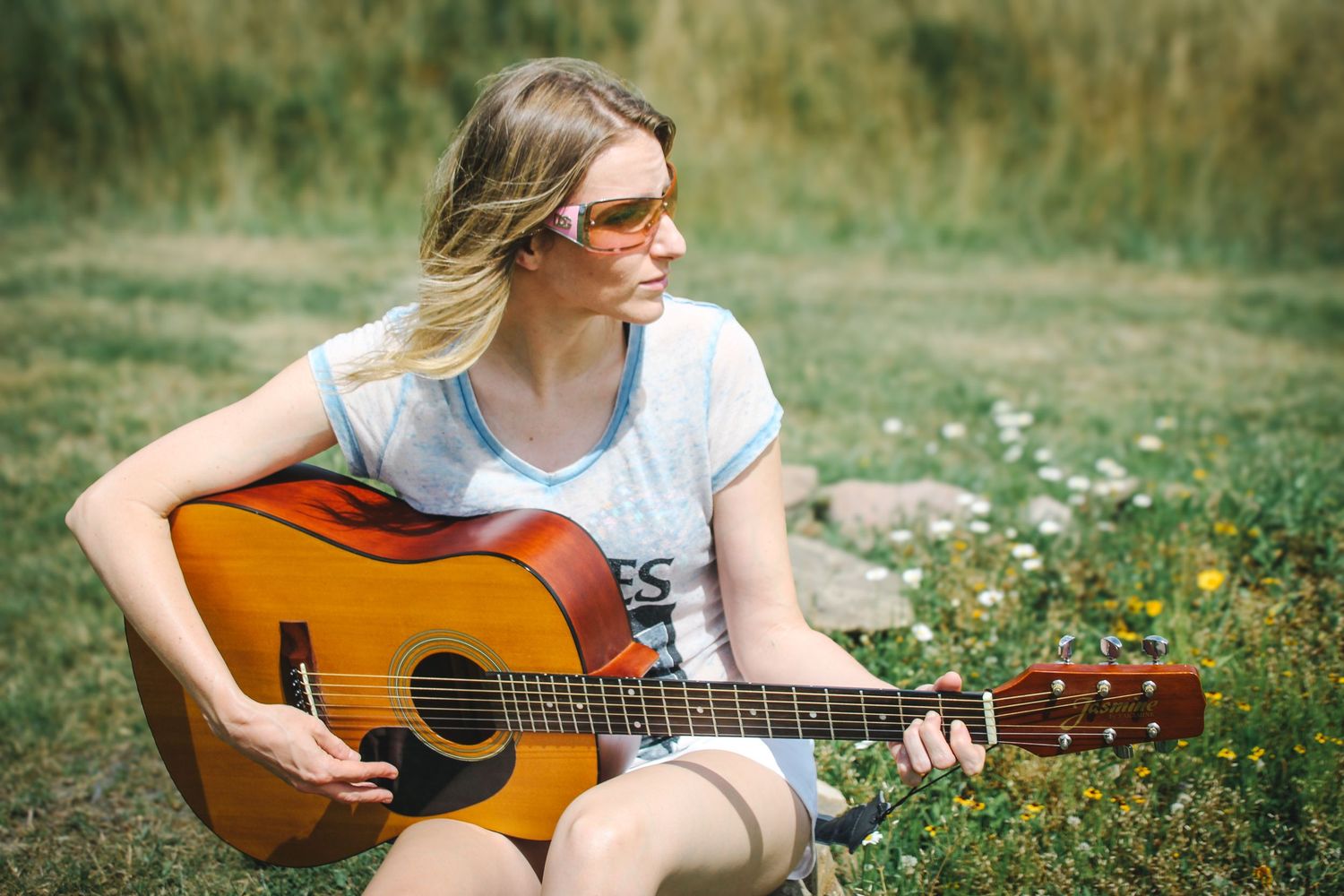 Someone plays an acoustic guitar while sitting in a wildflower meadow on a sunny summer day.