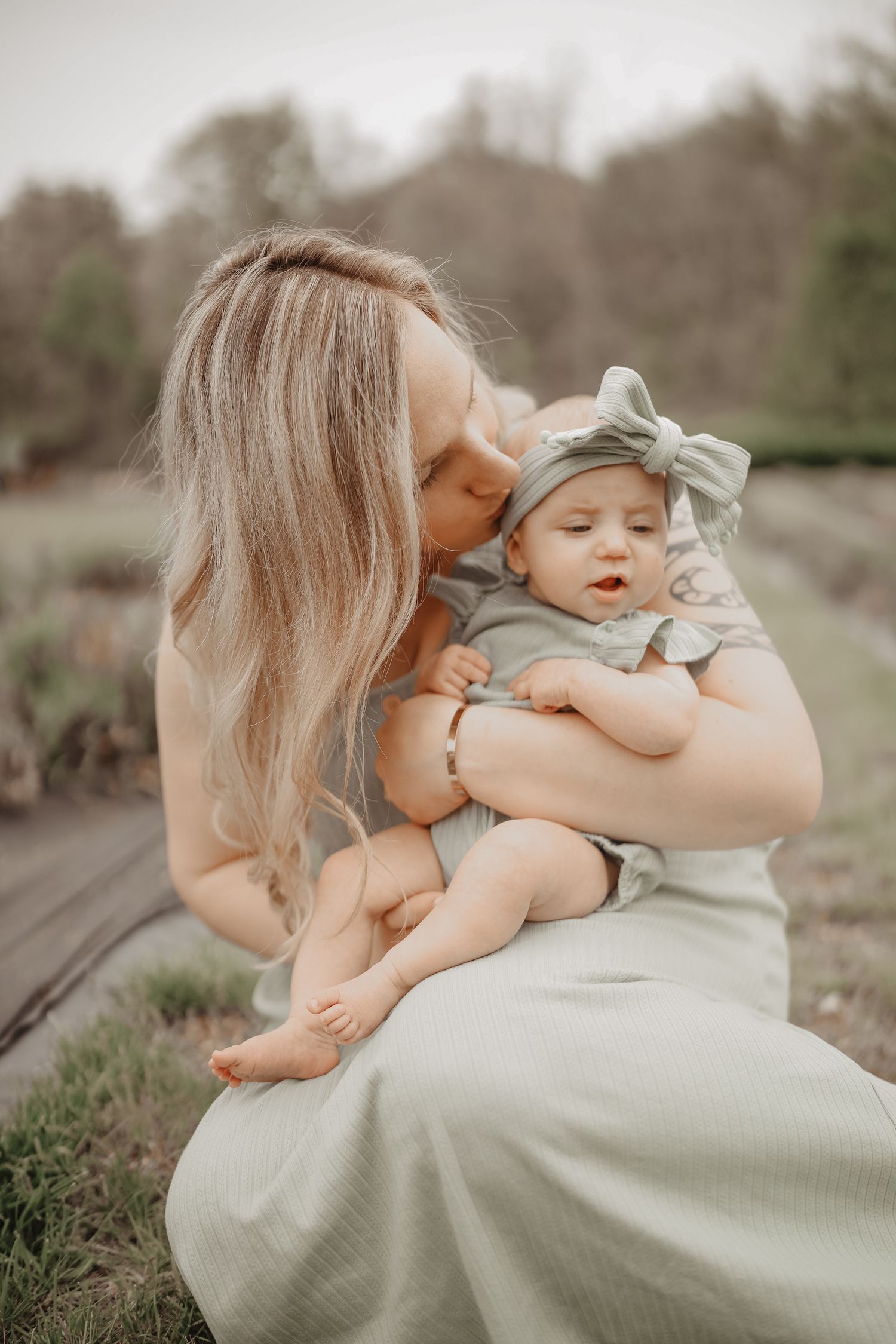 A tender moment captured outdoors showing affection between a parent and baby wearing matching neutral tones.