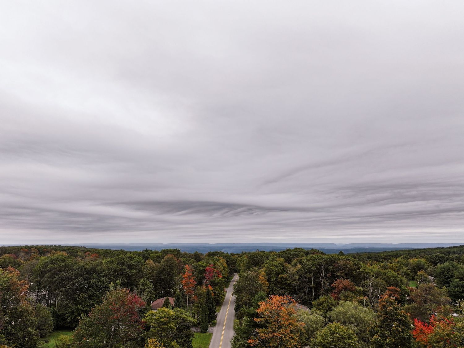 A panoramic view of autumn trees and winding roads stretches across a cloudy New England landscape.