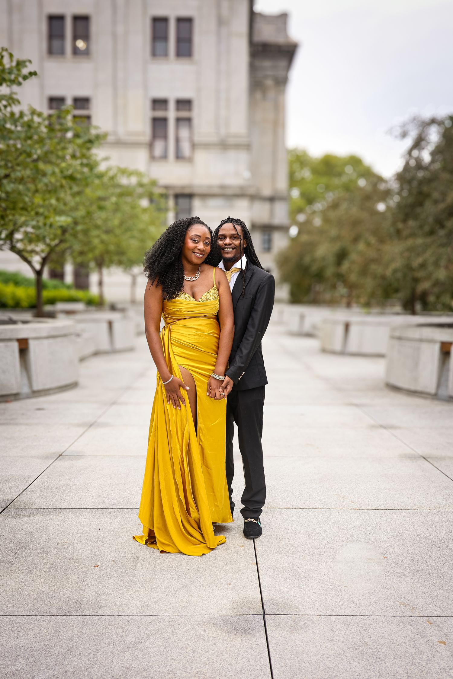 A couple shares a romantic moment on a concrete terrace, with the person in a vibrant yellow dress creating a striking contrast.