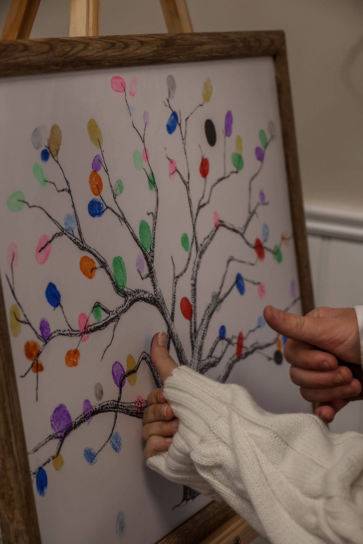 Hands in white knit gloves holding up colorful artwork featuring fingerprint birds on tree branches against a white background.
