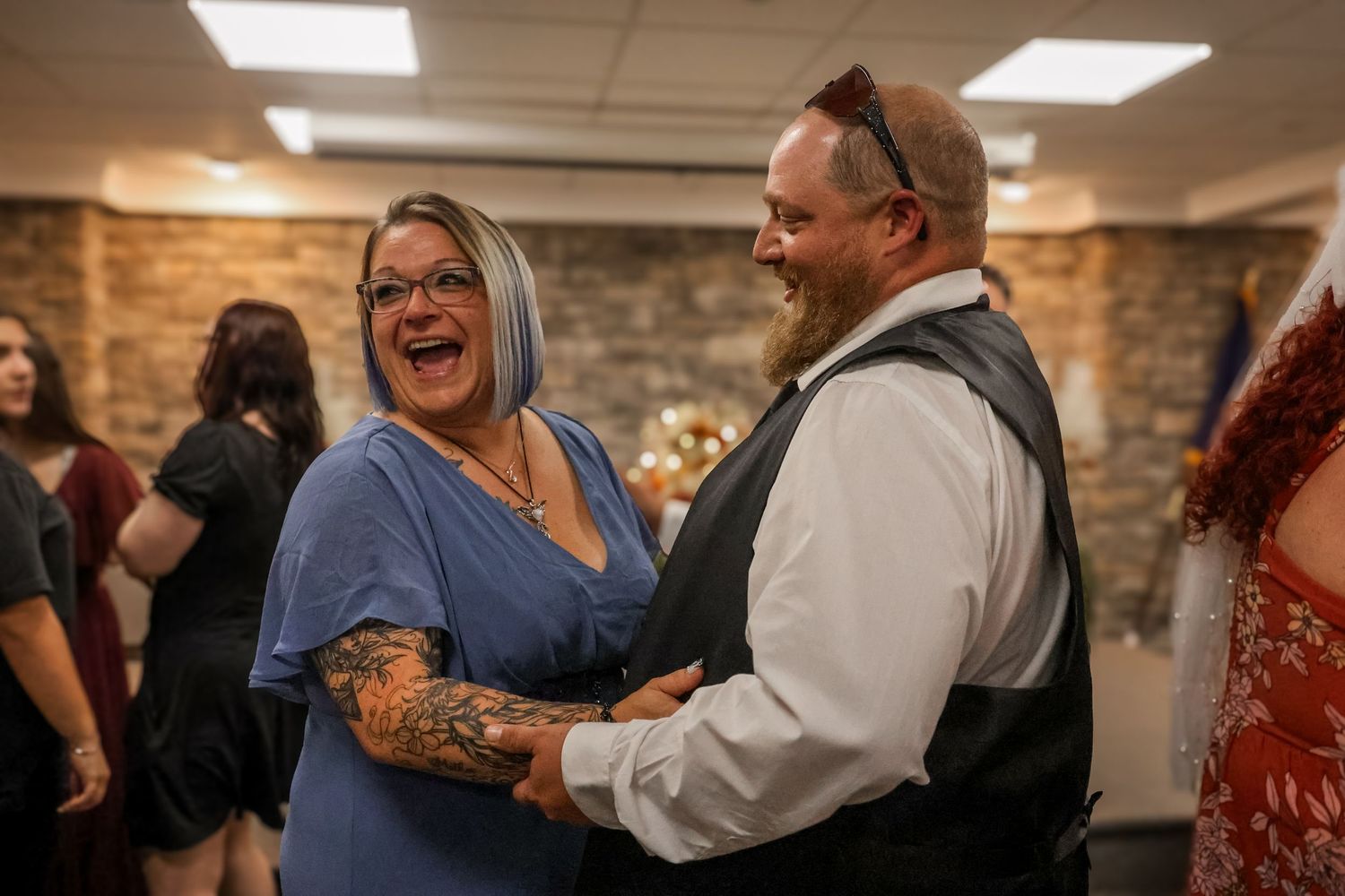 Two people share a joyful moment together while laughing during a social gathering in a room with stone walls.