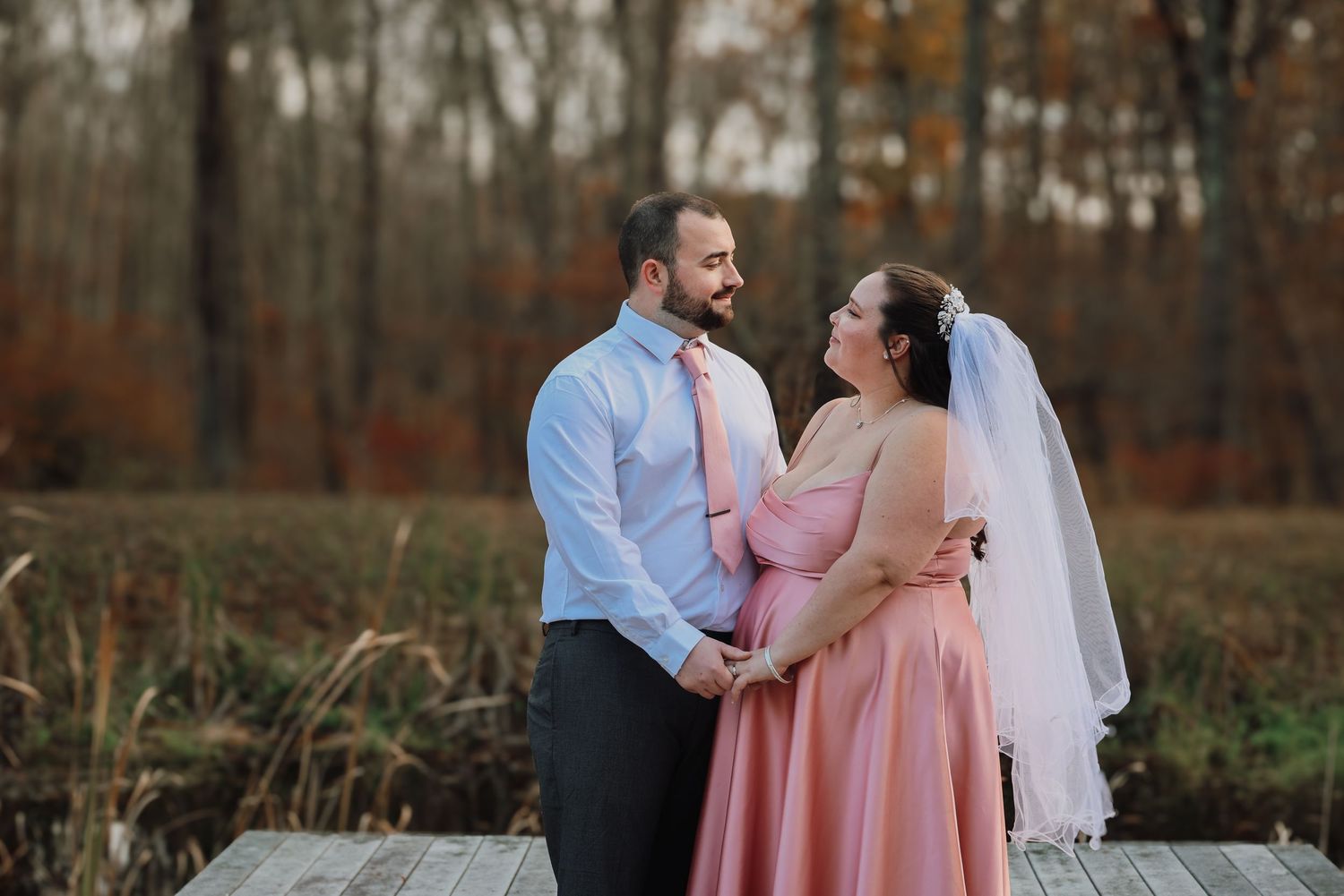 A couple in formal attire embraces in an autumn forest setting during a romantic outdoor photoshoot.