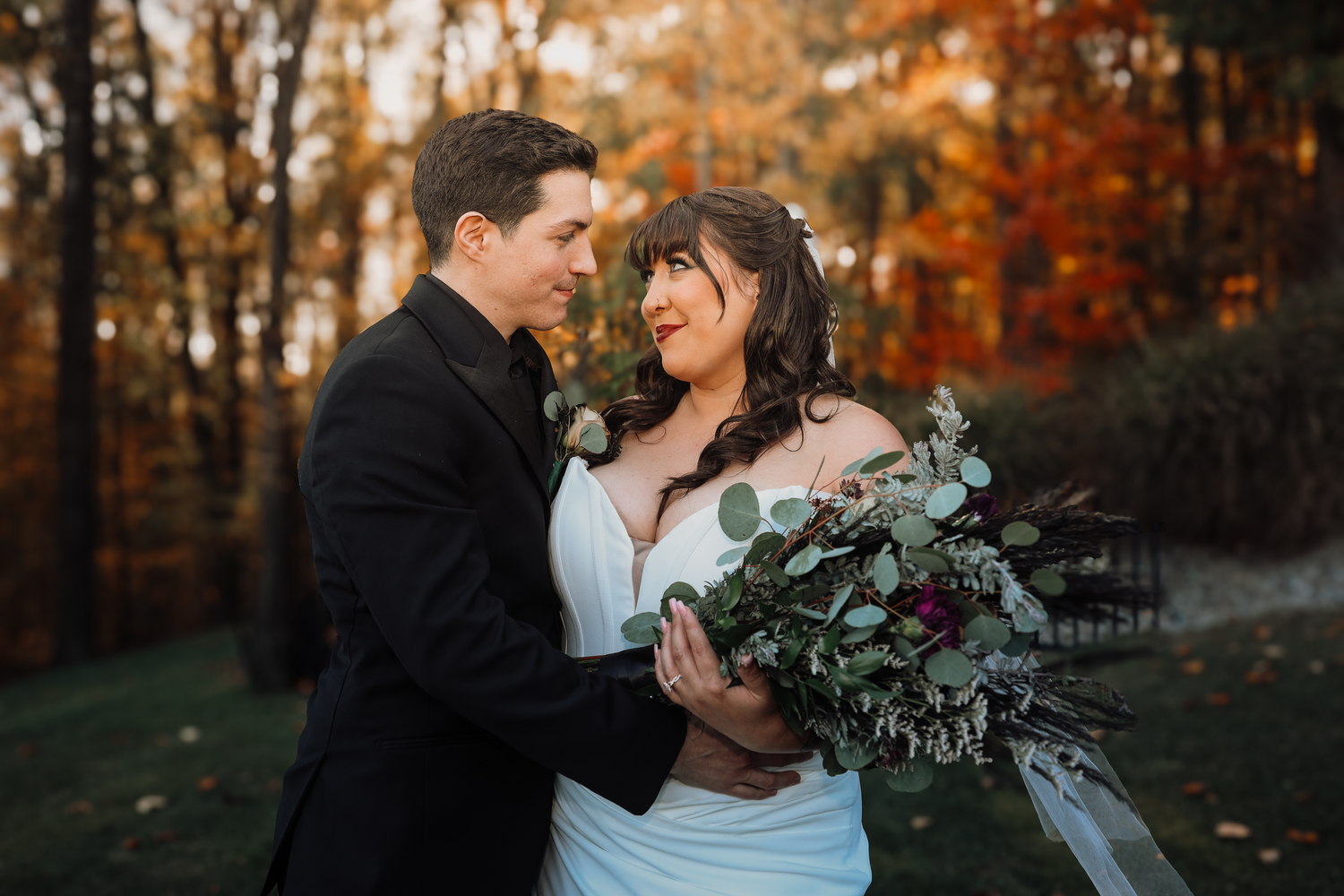 A couple embraces during an autumn wedding photoshoot in a forest with golden foliage at sunset.