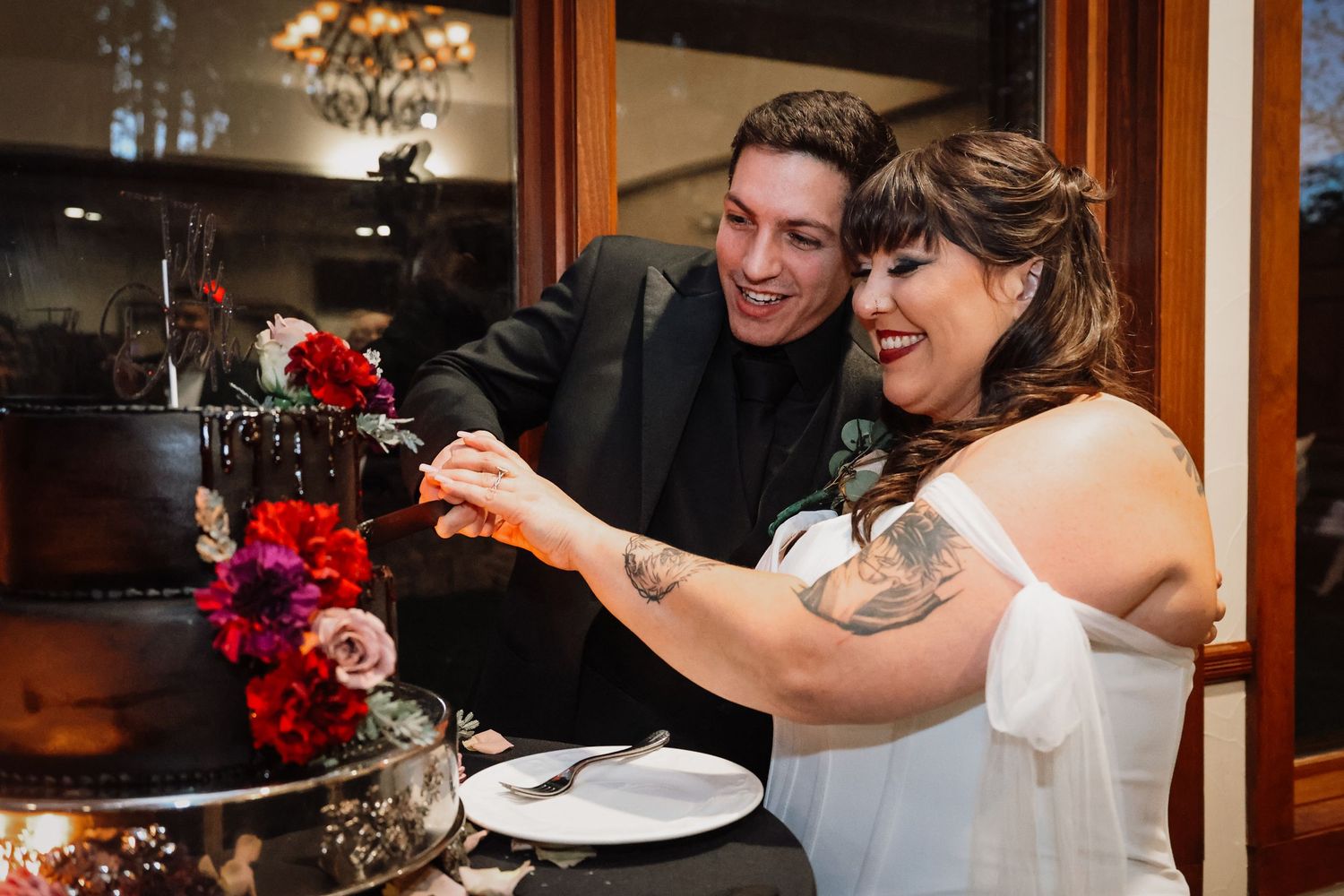 Couple shares a playful moment while cutting their wedding cake together at an indoor reception.