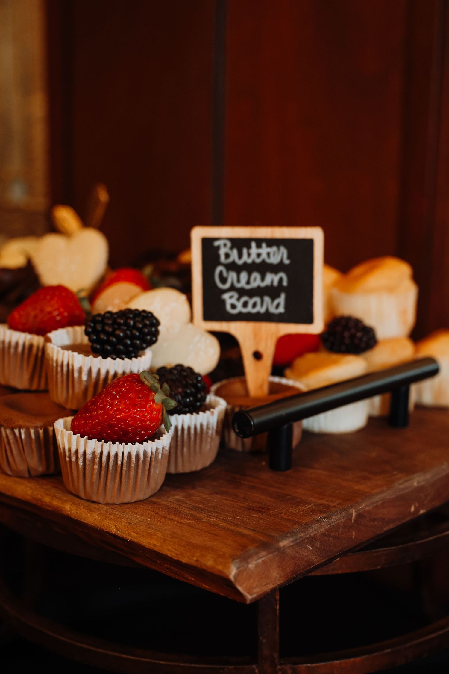 Fresh berries and chocolate cupcakes arranged on a rustic wooden serving board in moody lighting.