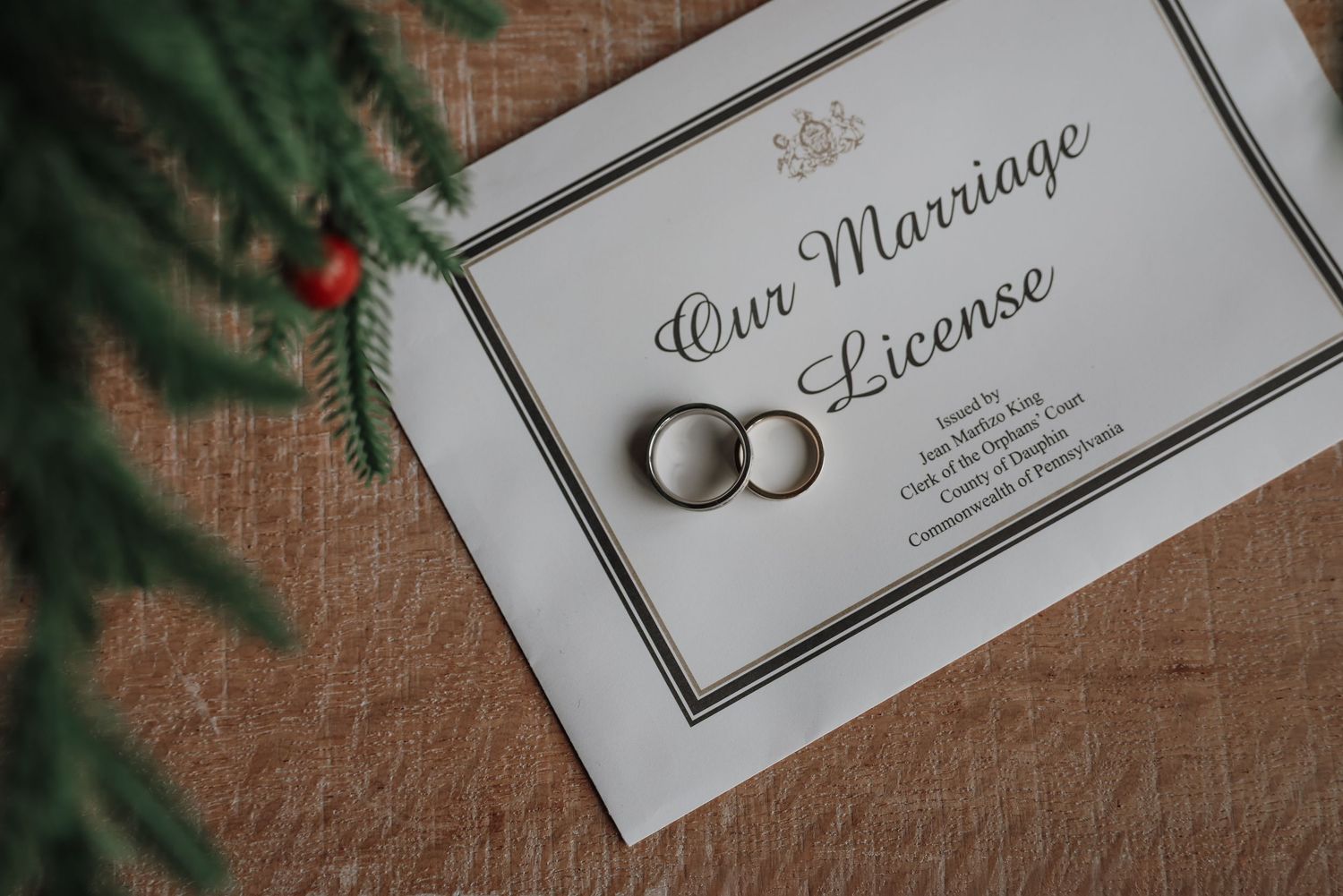 Wedding invitation cards and silver rings displayed among evergreen branches and rustic burlap background.