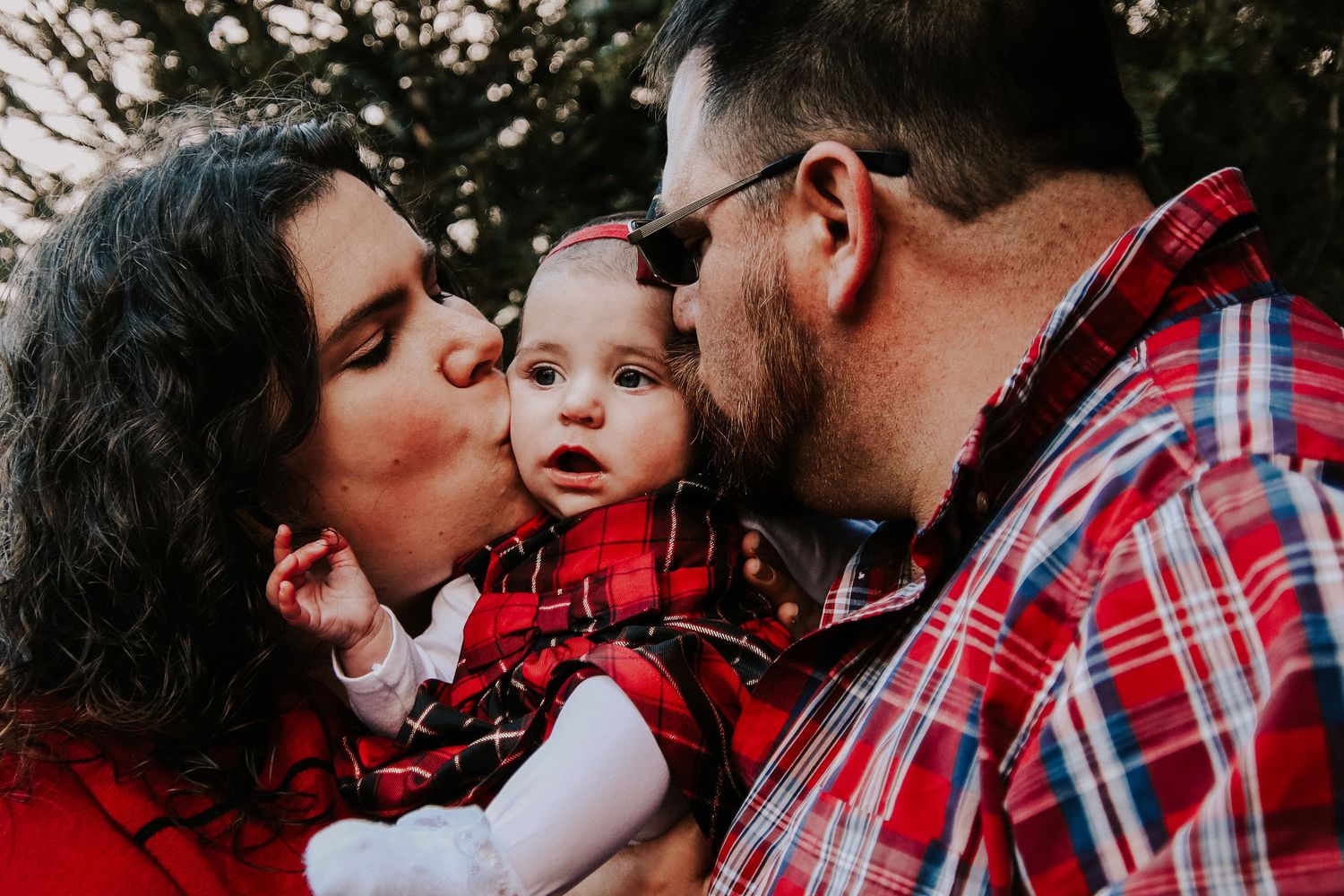A family wearing red and plaid shares a tender moment together outdoors during a photo session.