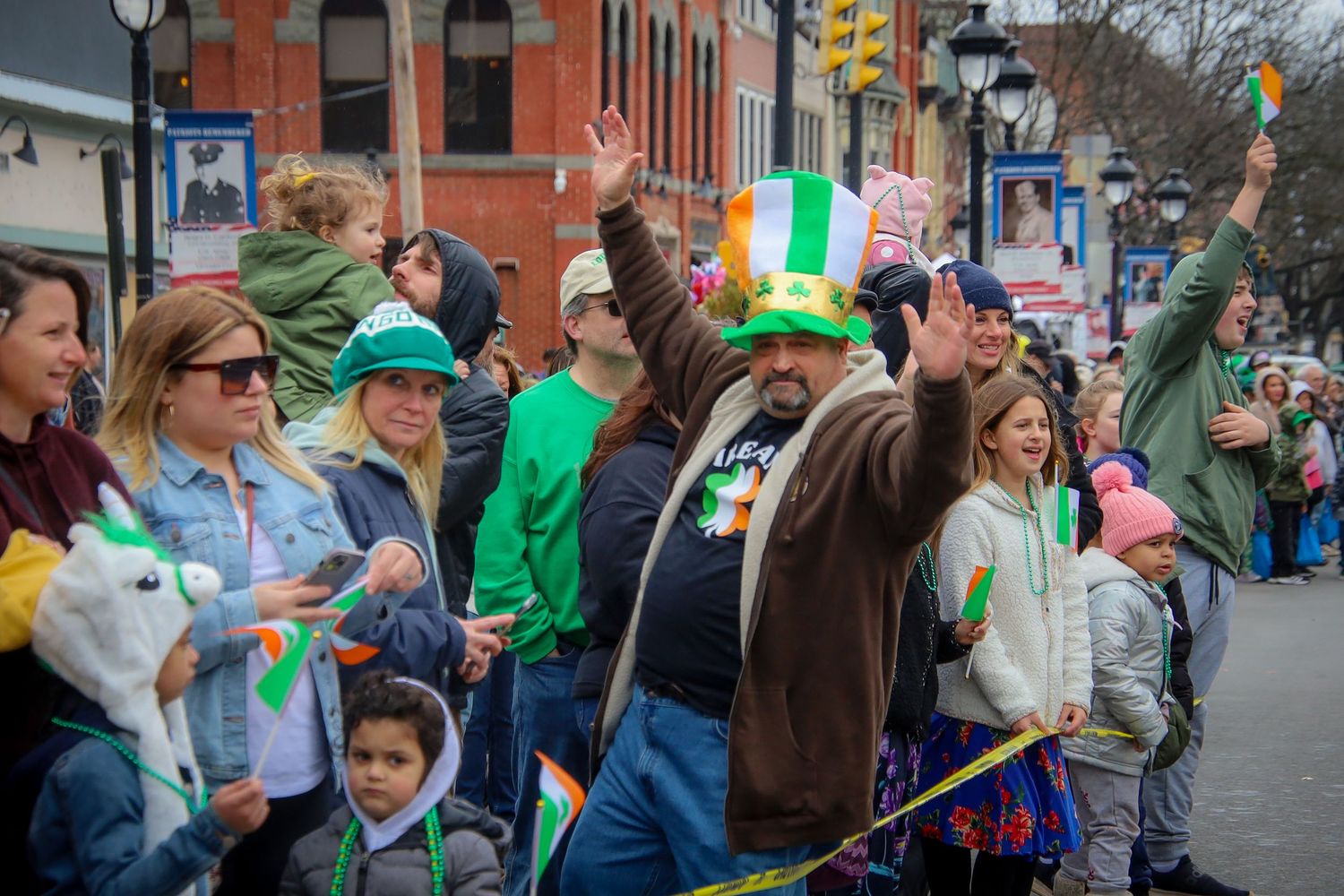 A crowd of festive parade spectators wearing green attire and accessories during a St Patrick's Day celebration.