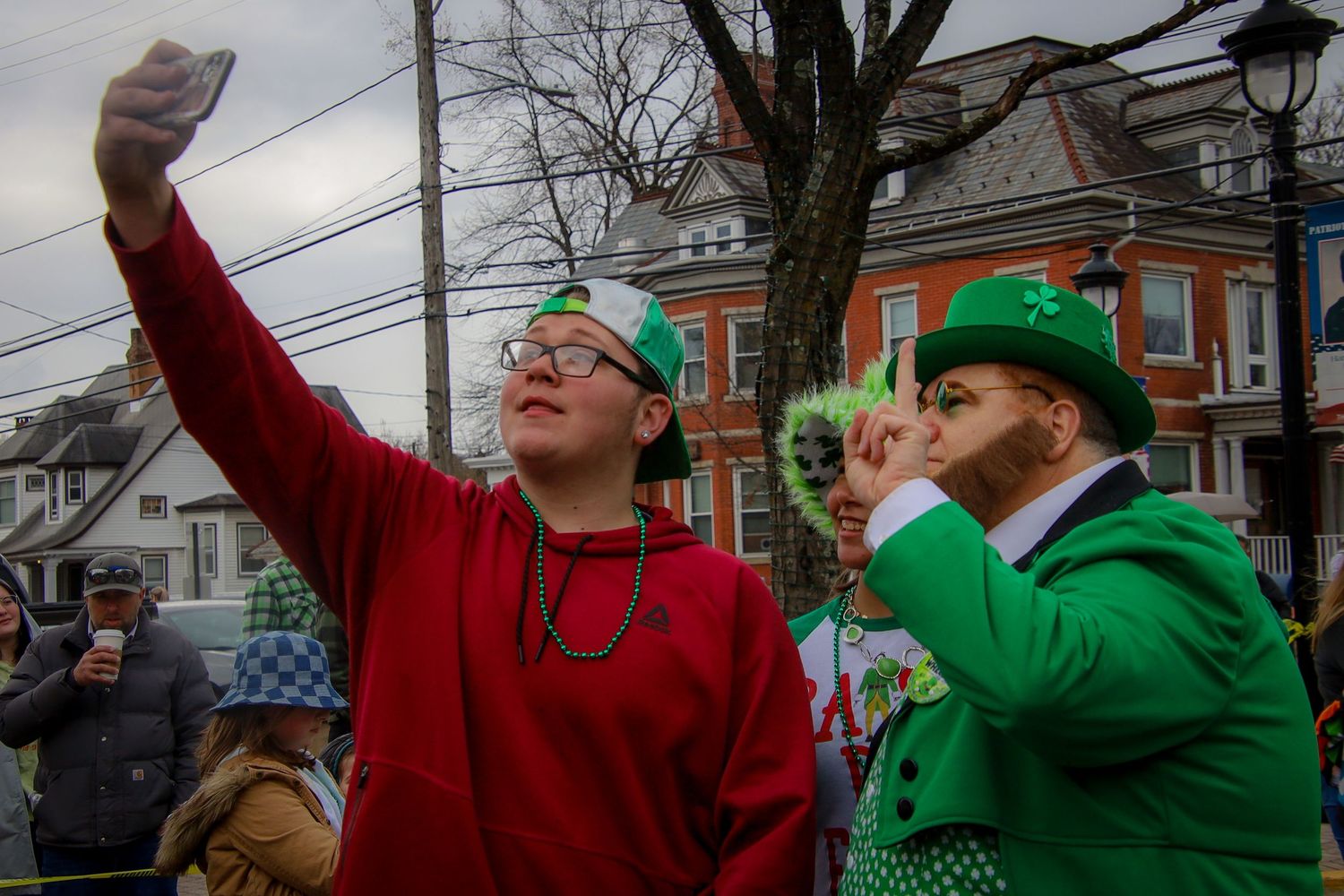 Revelers in red and green attire celebrate at a festive St. Patrick's Day parade in an urban neighborhood setting.