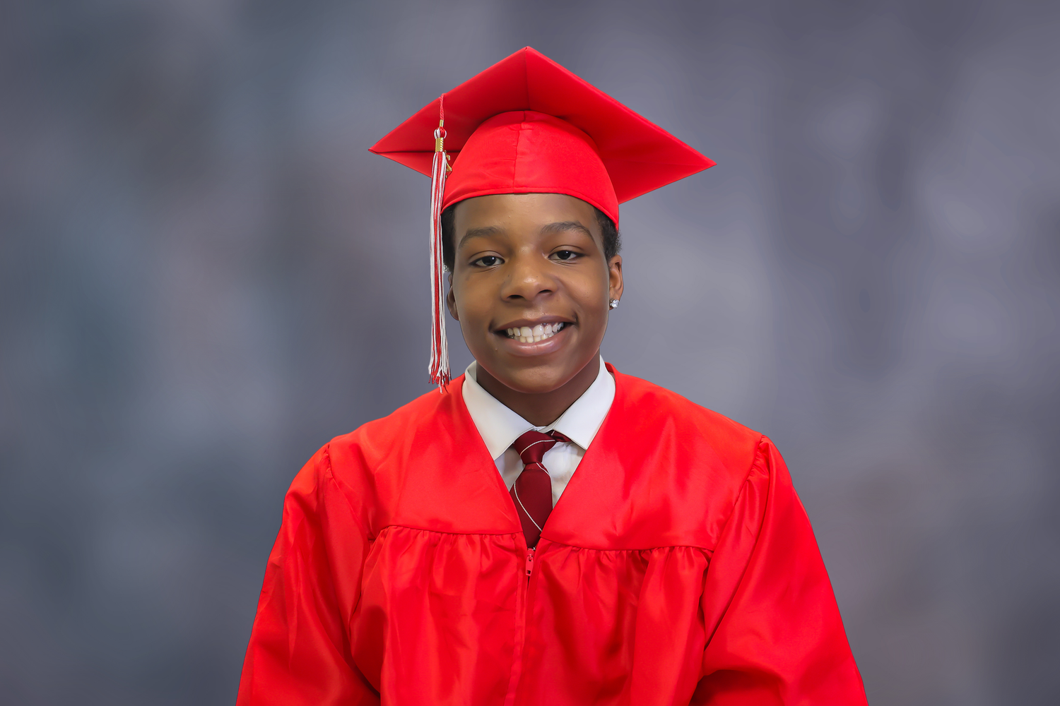 Graduate in bright red cap and gown poses for professional portraits against gray background.
