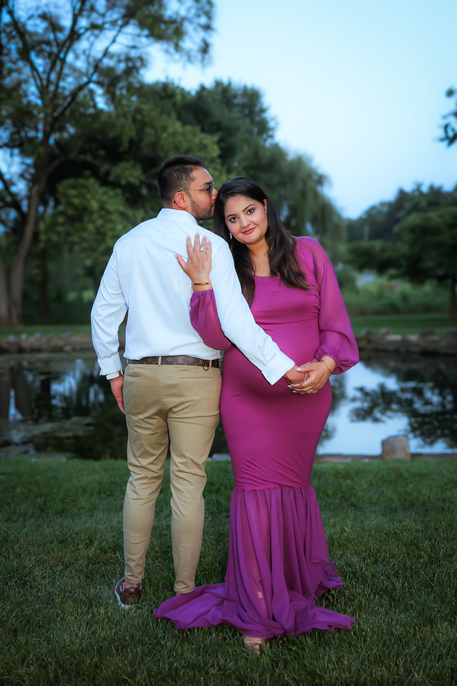A couple in matching white and khaki outfits with a purple dress pose lovingly together on grass during a photo session.