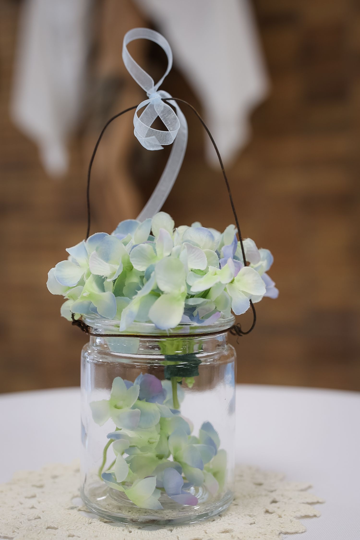 A delicate glass jar filled with white and pale blue hydrangea flowers tied with a white ribbon creates an elegant centerpiece.