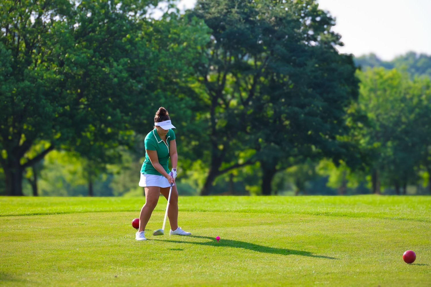 A golfer in blue and white attire takes a swing on a lush green golf course on a sunny day.