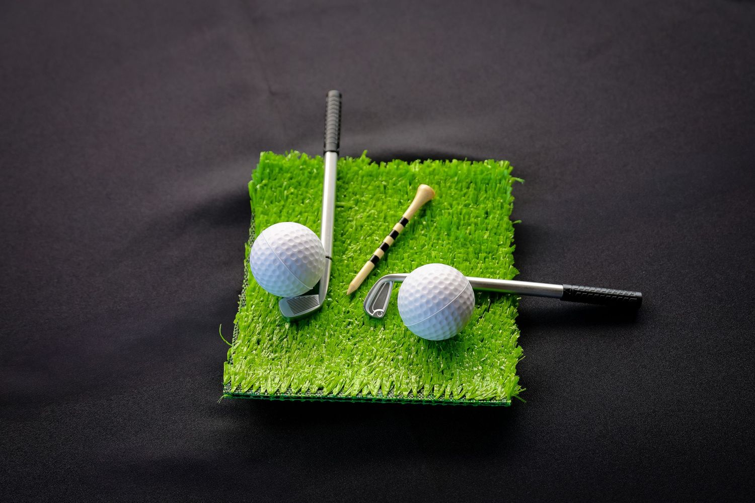 Golf ball and tee positioned on artificial turf with dark background in a creative composition.