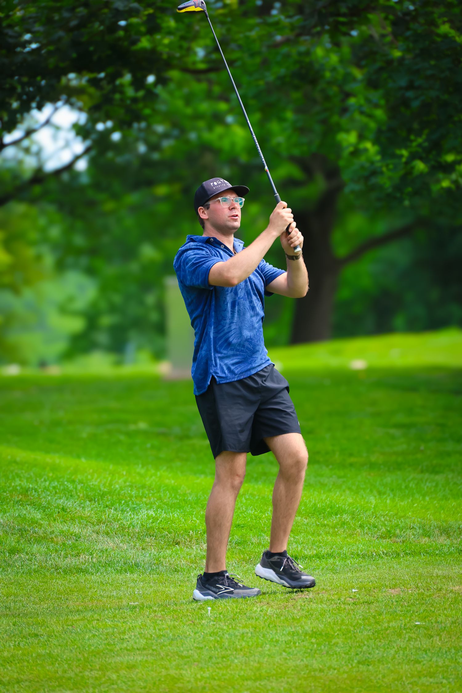 Golfer in blue shirt and shorts takes a stance on green grass course preparing for a shot.
