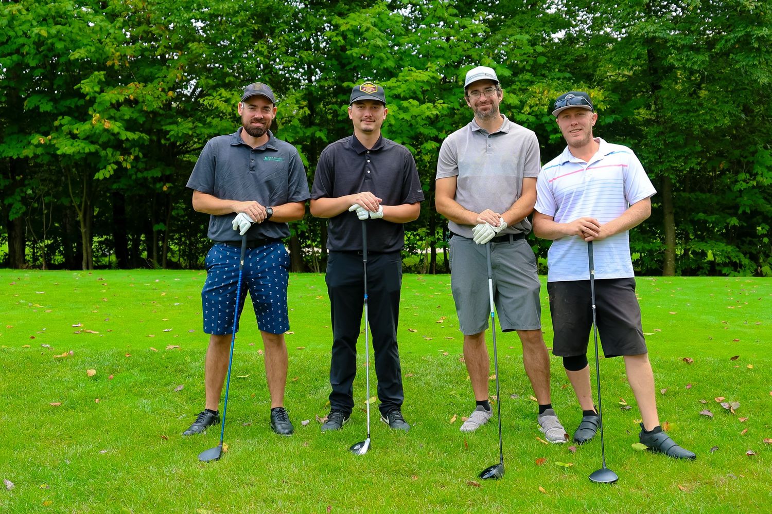 Four golfers stand together on a lush green course holding their clubs during a round of golf.