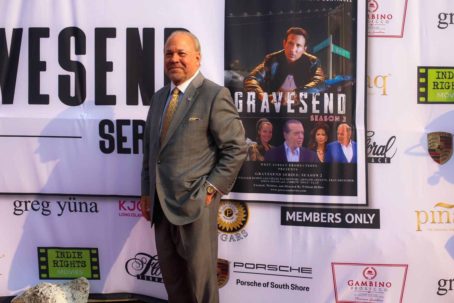 People posing against a wall covered with event posters and promotional materials at what appears to be a media event.