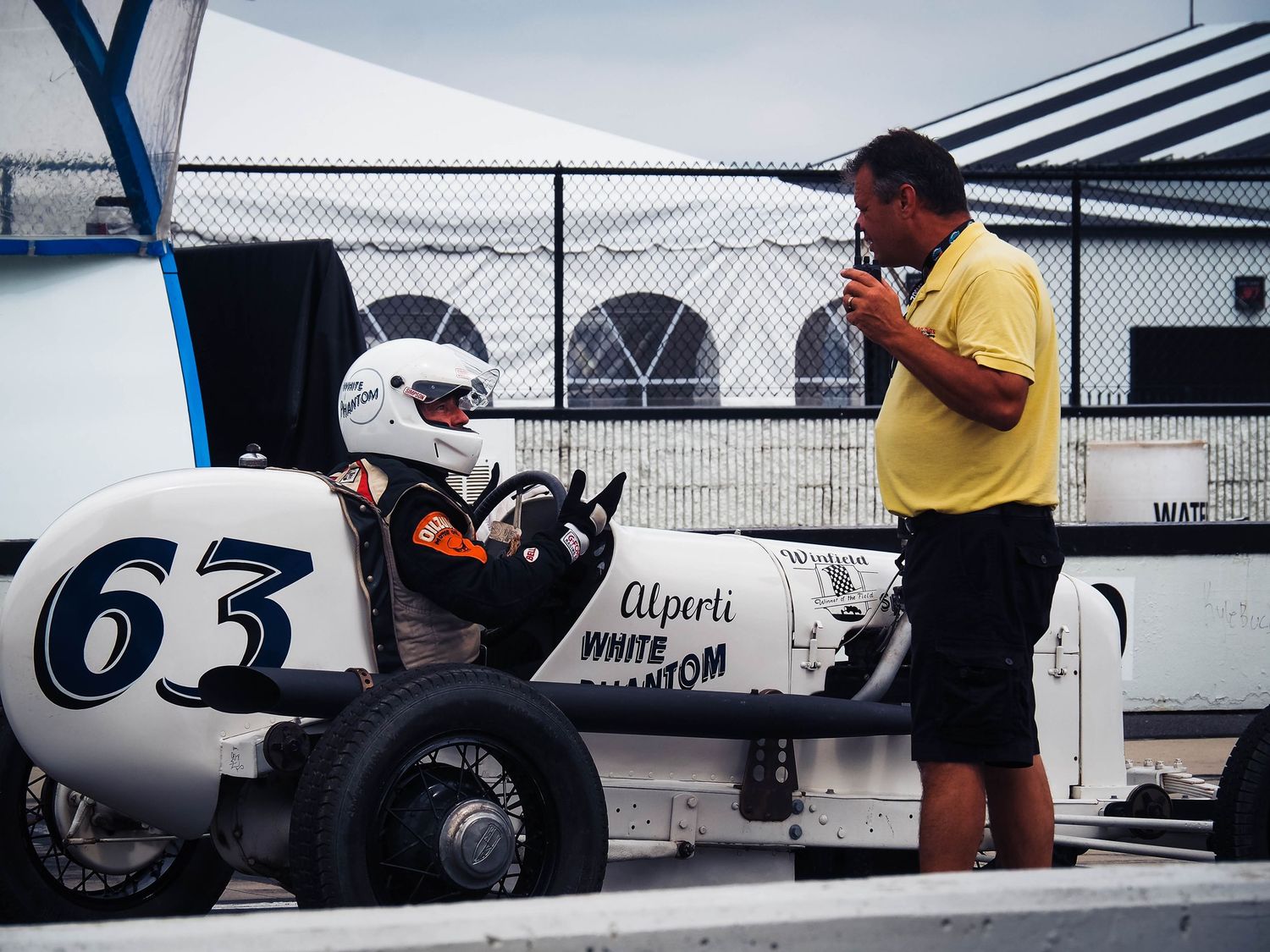 Vintage race car mechanics work on a classic Formula One vehicle in a pit garage during maintenance.