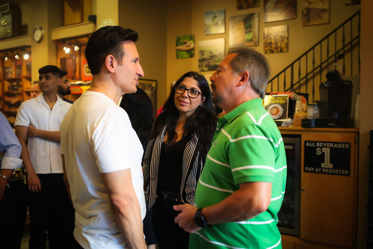 Three people engaged in conversation at a casual gathering inside a restaurant with framed photos on walls.