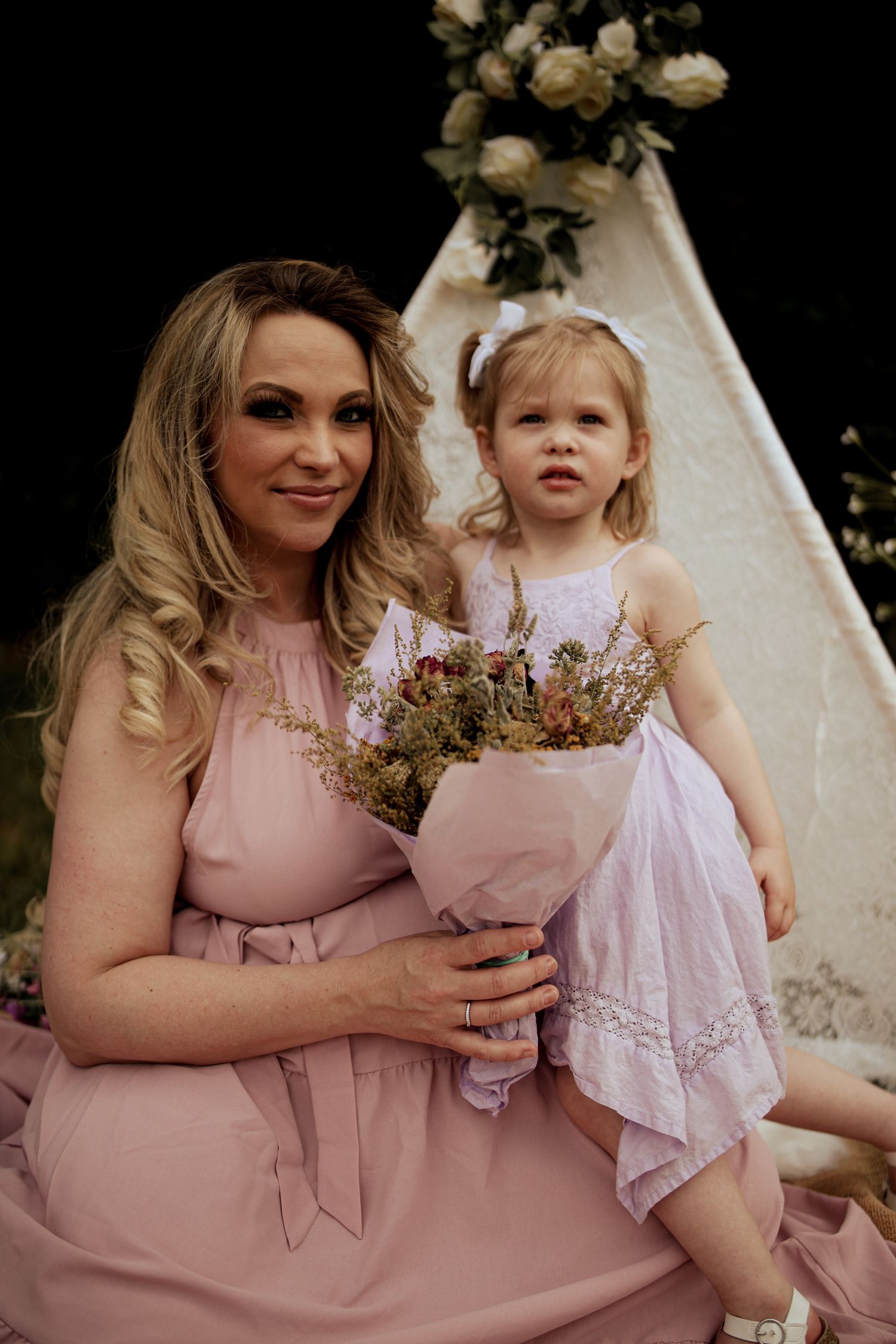 Mother and daughter in pink dresses share tender moments during outdoor photo session near white tent.