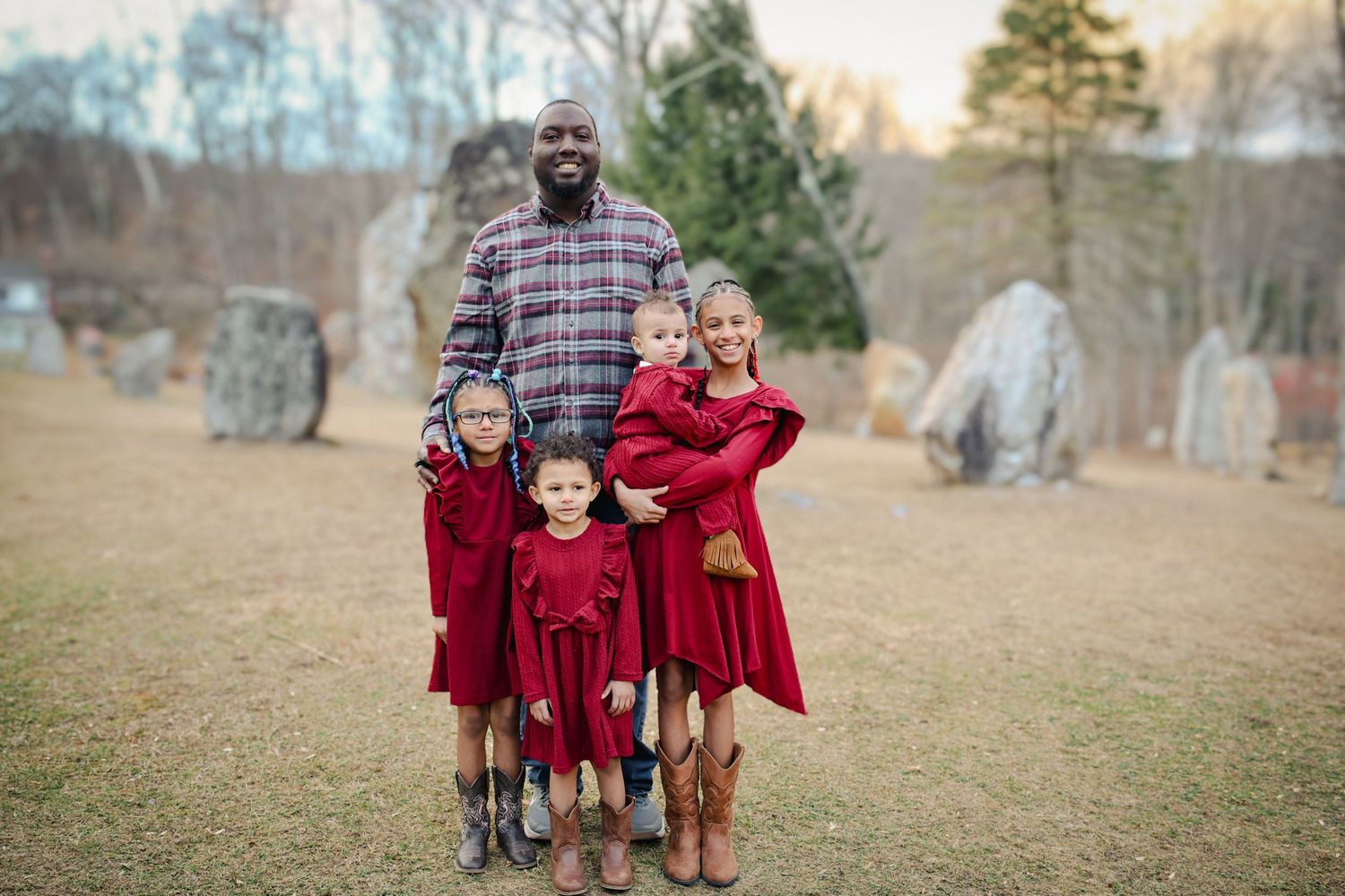 A family wearing coordinated burgundy outfits poses together in a rustic outdoor setting during autumn.