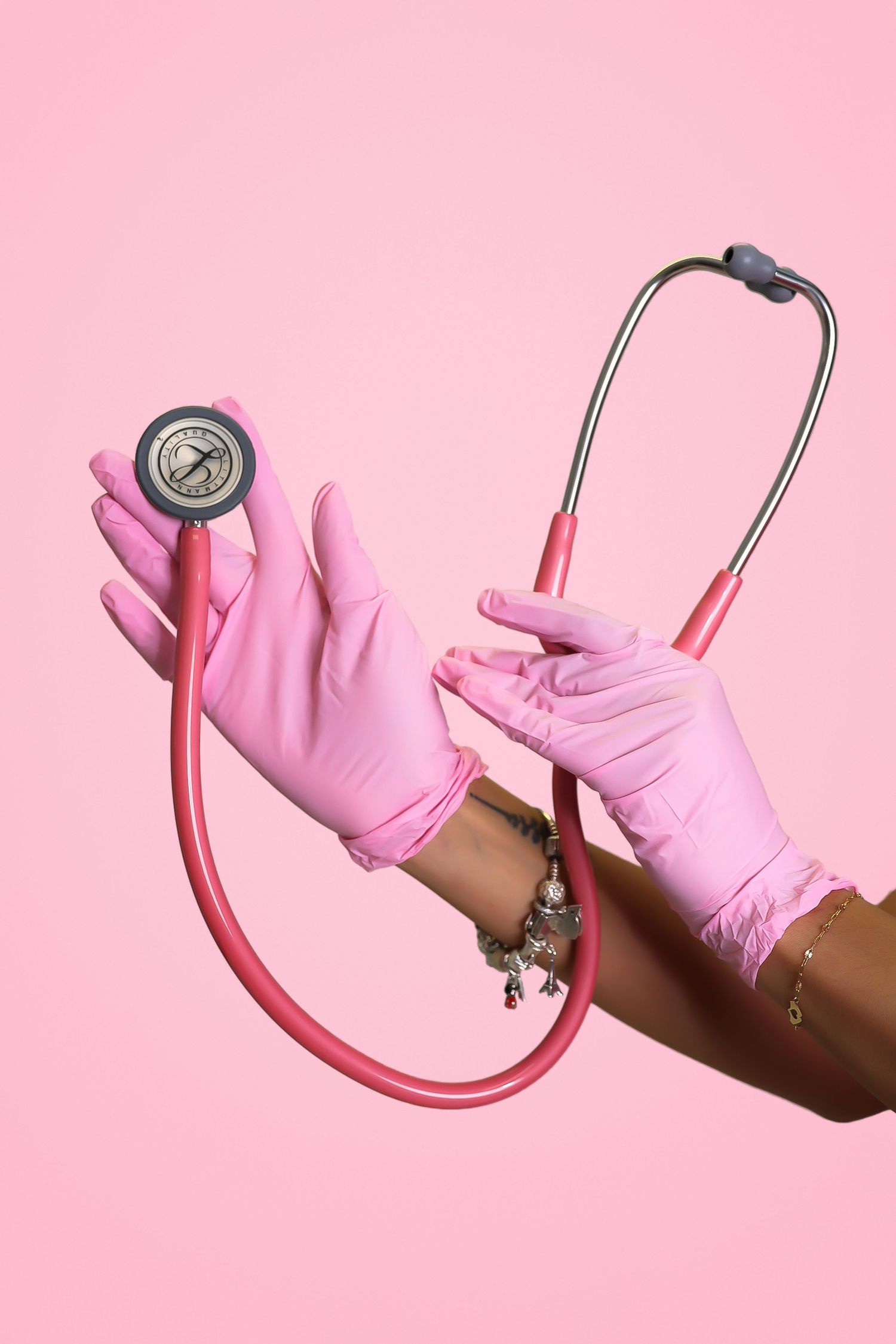 Hands in pink latex gloves holding a pink stethoscope against a pink background.