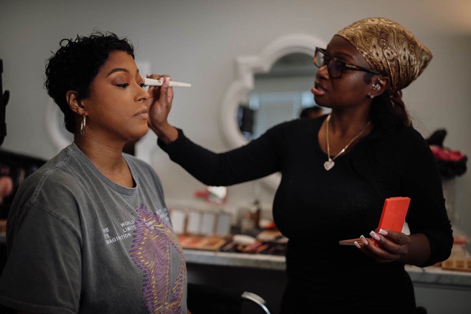 makeup artist applying foundation to a woman's face using a brush at a beauty salon.