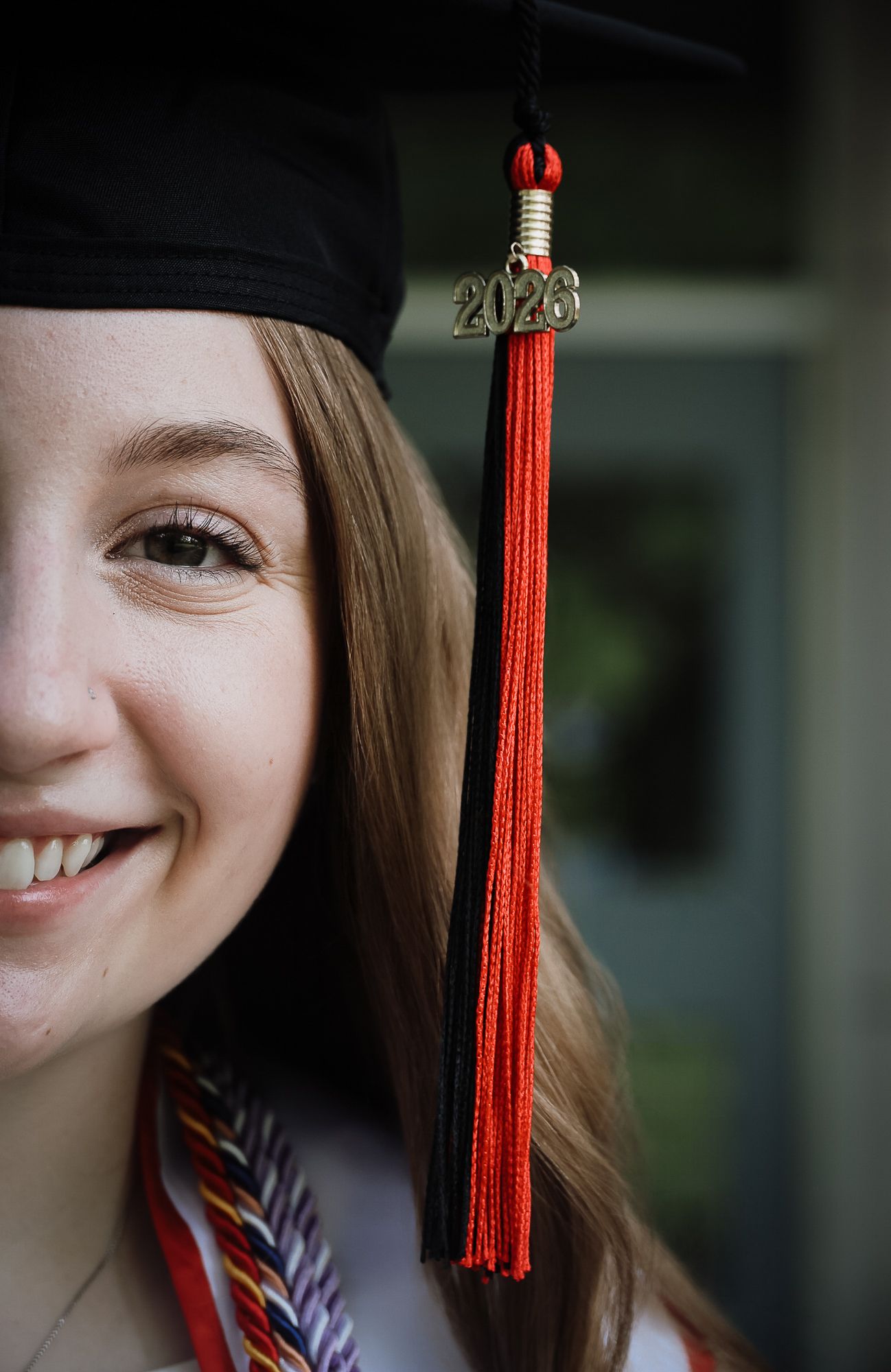 Smiling young woman in black graduation cap with red 2020 tassel celebrating her academic achievement.