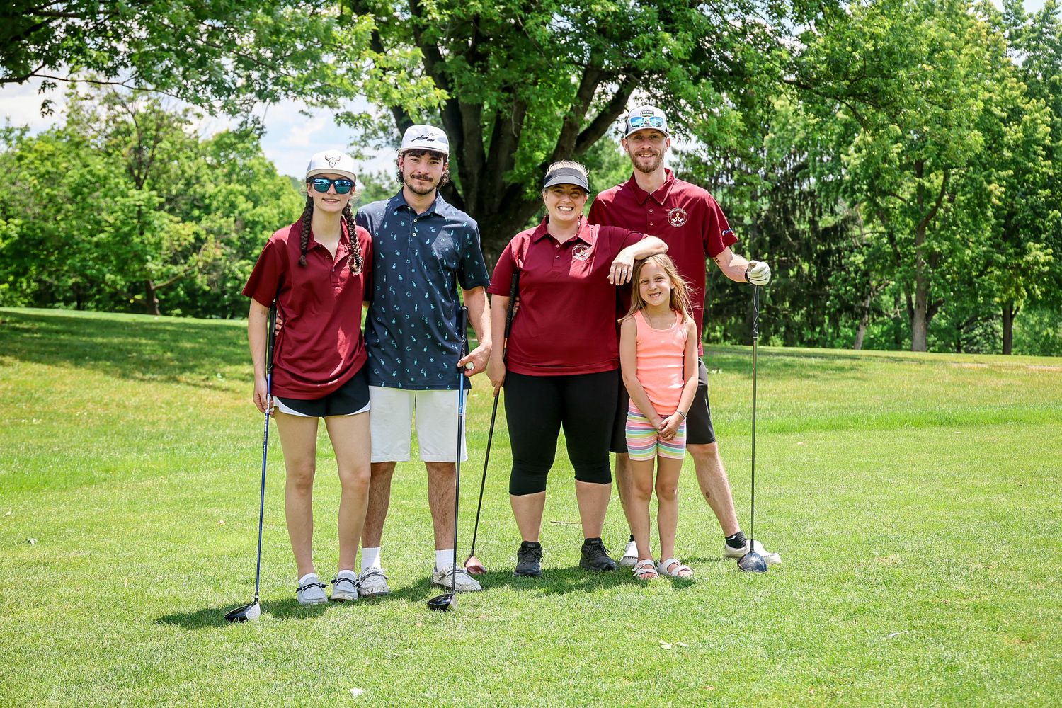 Group of five golfers in matching maroon shirts posing on a green golf course.