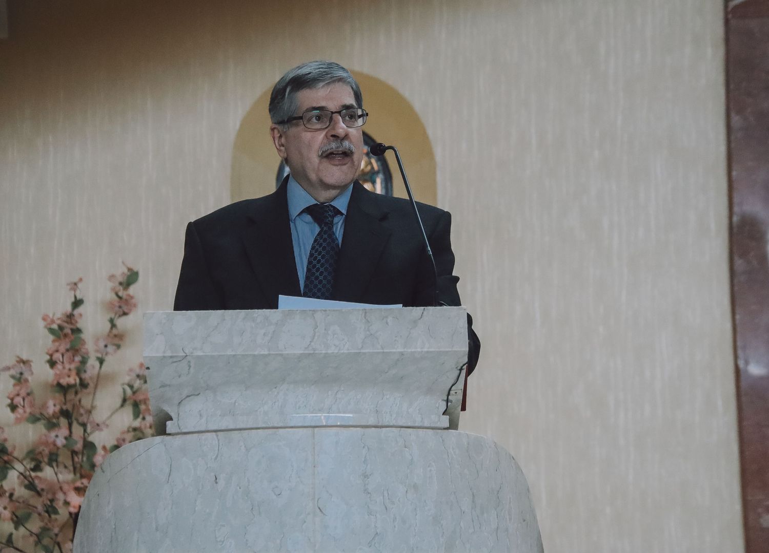 A speaker stands at a podium delivering remarks during what appears to be a formal presentation or ceremony.