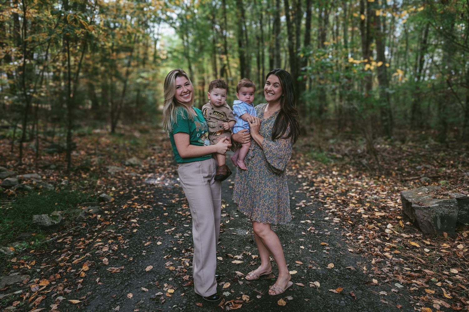 Family walks together on autumn forest trail covered in fallen leaves during outdoor photo session.