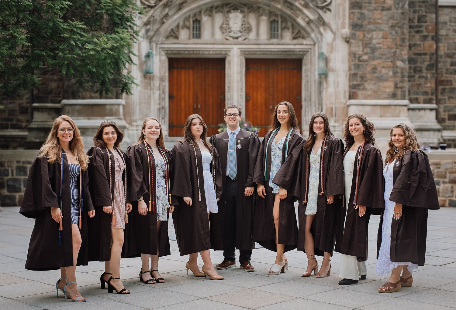 A panoramic sequence of graduates in black academic regalia posing together on stone steps of a historic building.