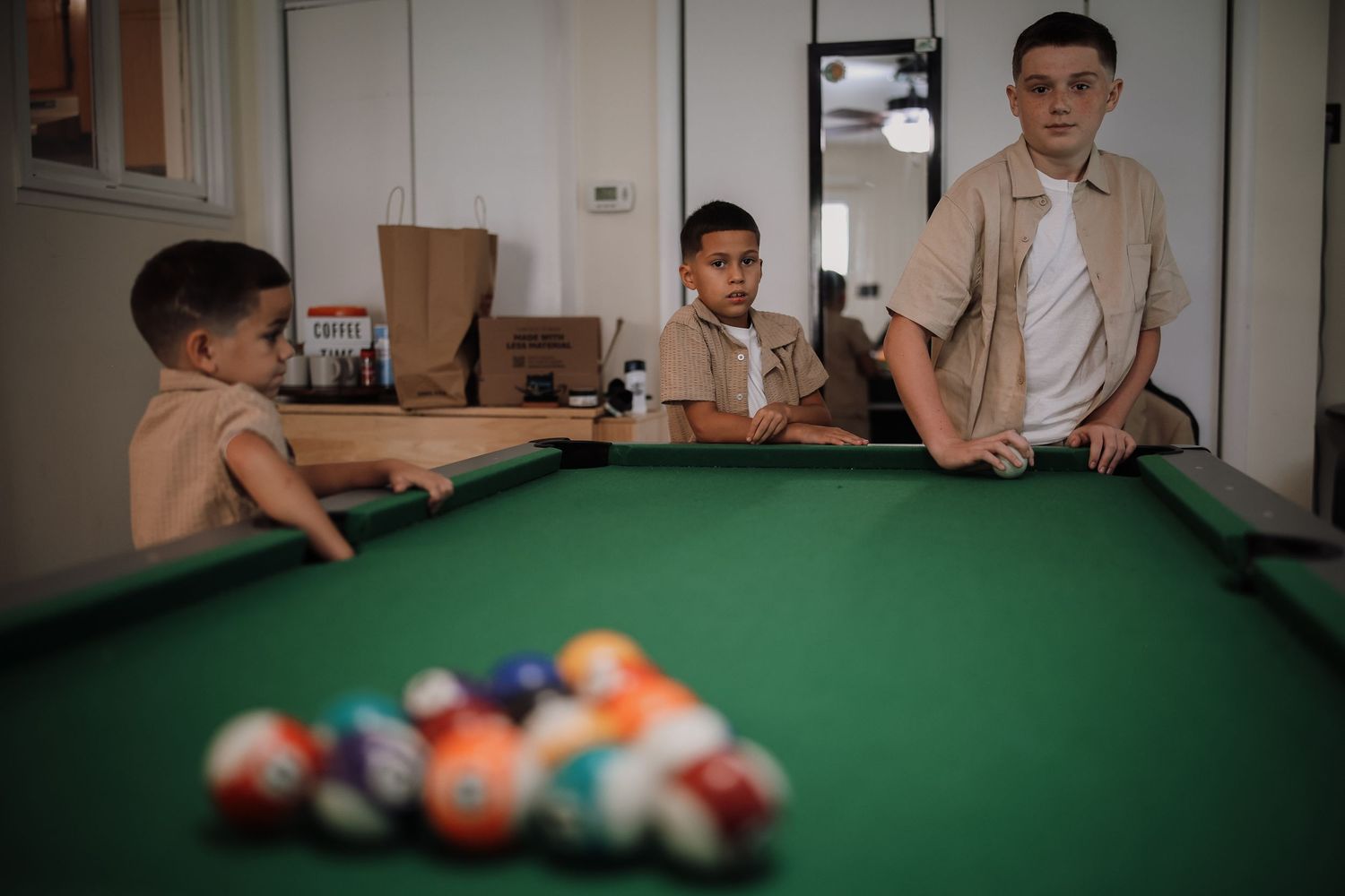 People playing pool at a green felt table with billiard balls scattered across the surface.