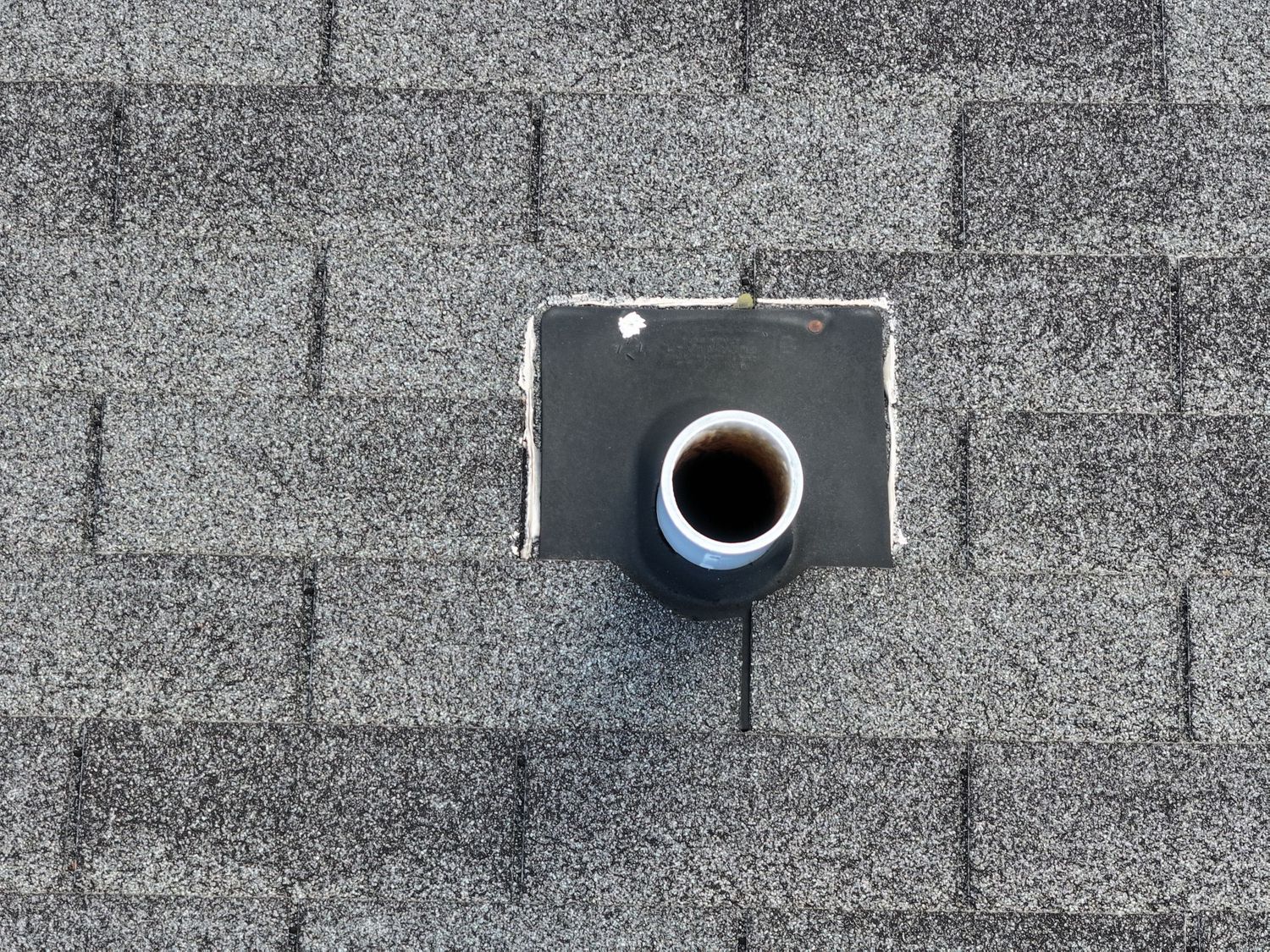 Black plumbing vent pipe protruding through gray asphalt shingles on a residential roof.