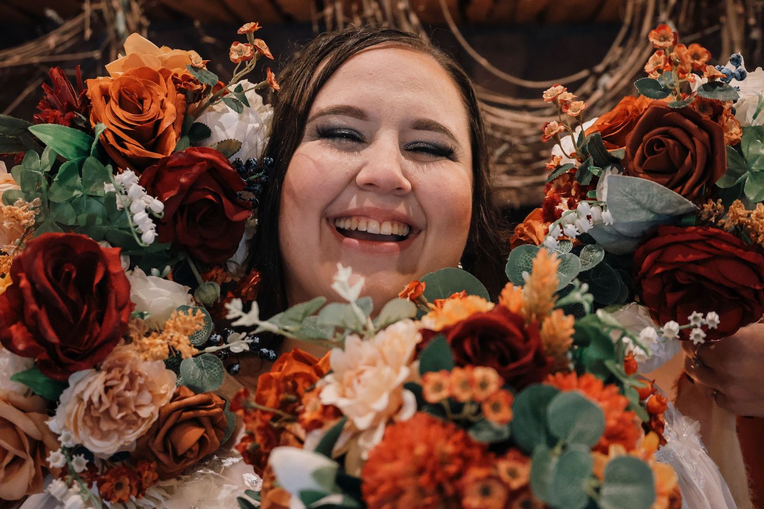 A vibrant wedding bouquet featuring orange and burgundy flowers with sage green foliage against a dark background.