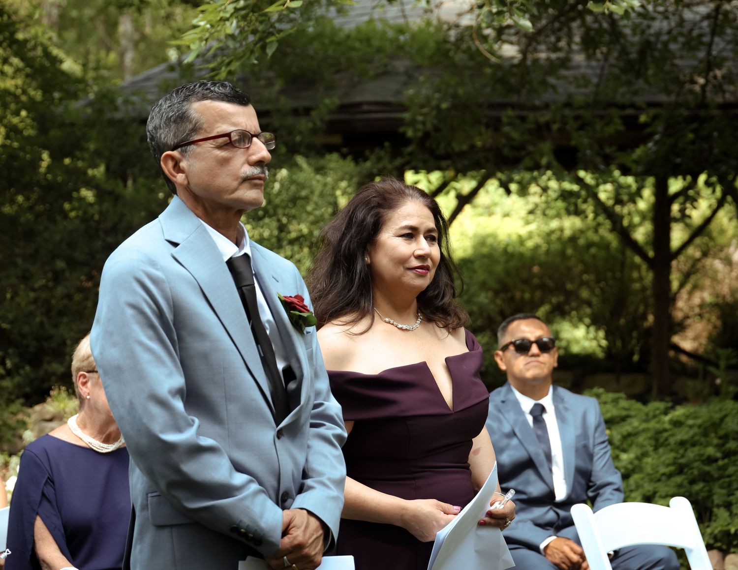 Wedding guests dance together at an outdoor reception in a garden setting.