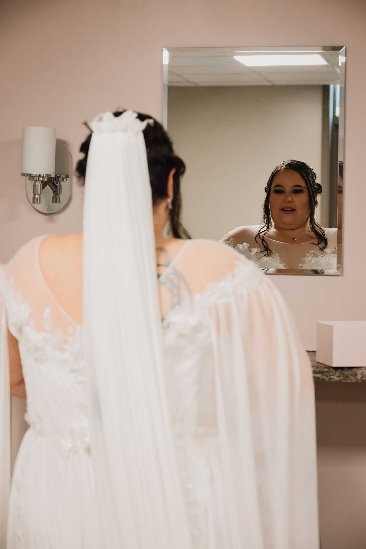 A bride in a white wedding dress with a long flowing veil is seen from multiple angles in a mirrored room.