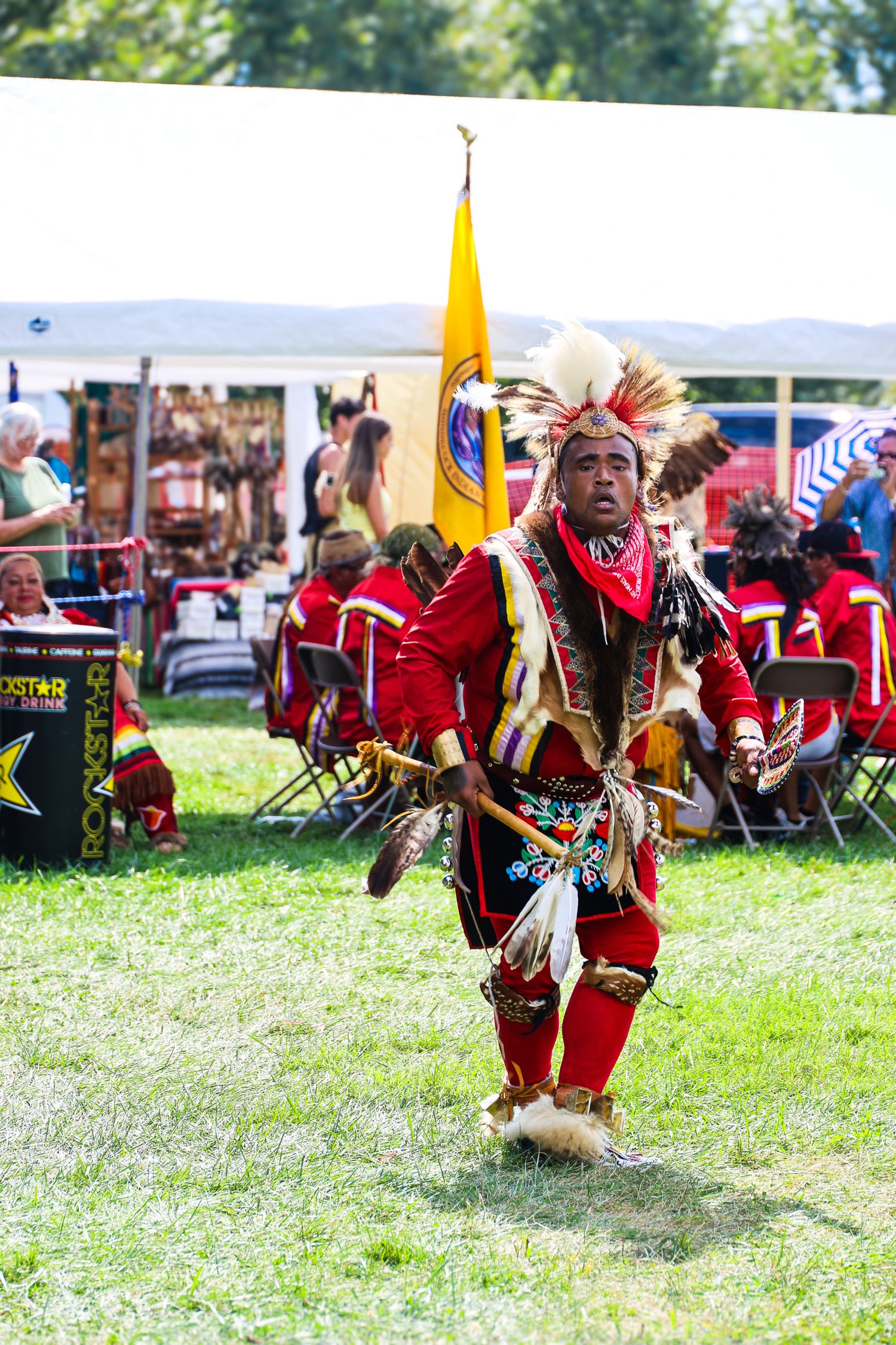Native American dancers perform traditional dances in vibrant red regalia at an outdoor cultural festival.