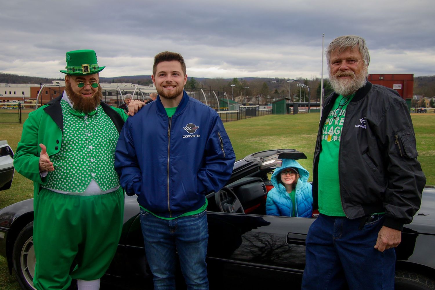 Group wearing blue jackets and green St. Patrick's Day outfits pose together at an outdoor gathering.