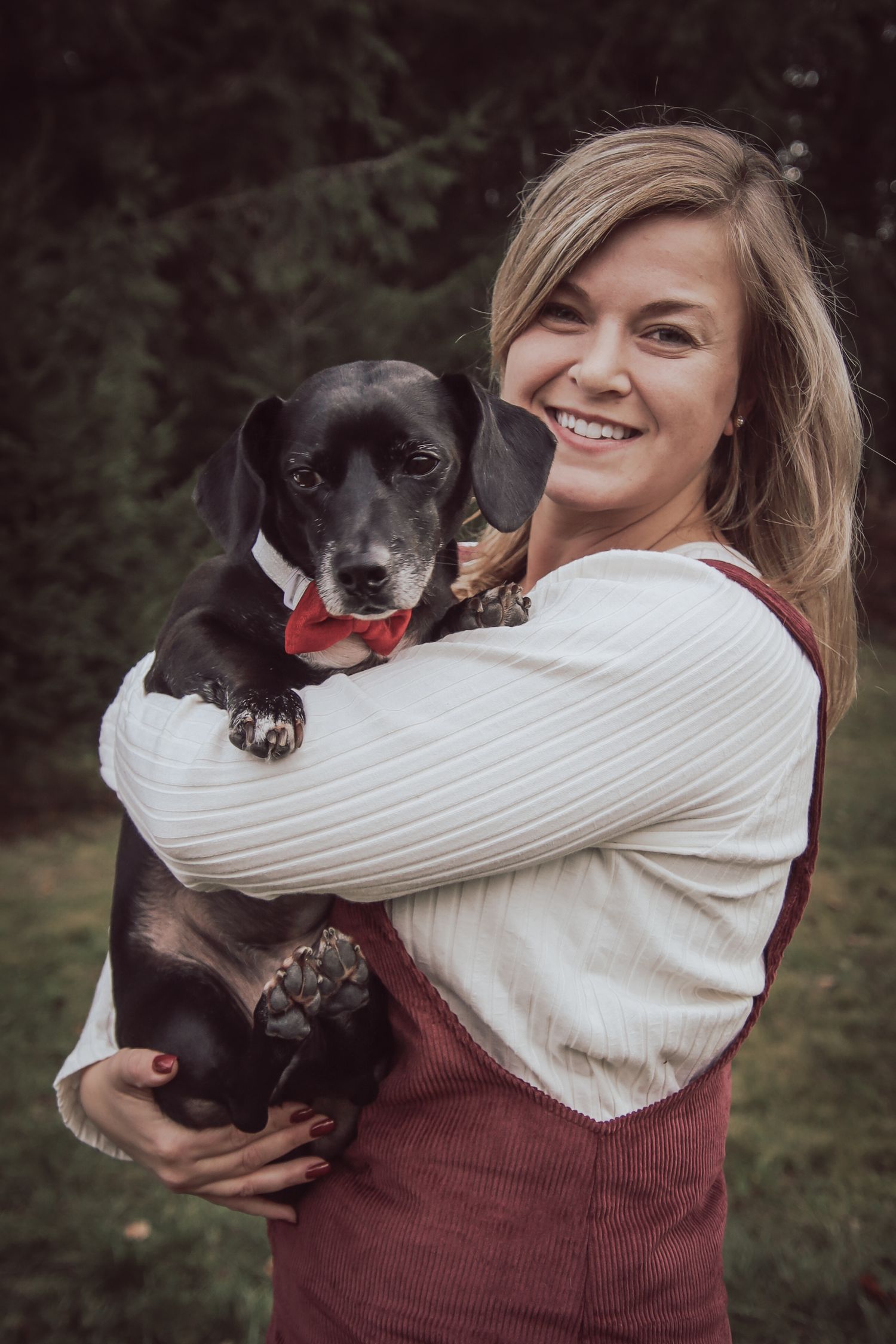 A person in a burgundy and white sweater holds a small black dog in a series of affectionate poses outdoors.